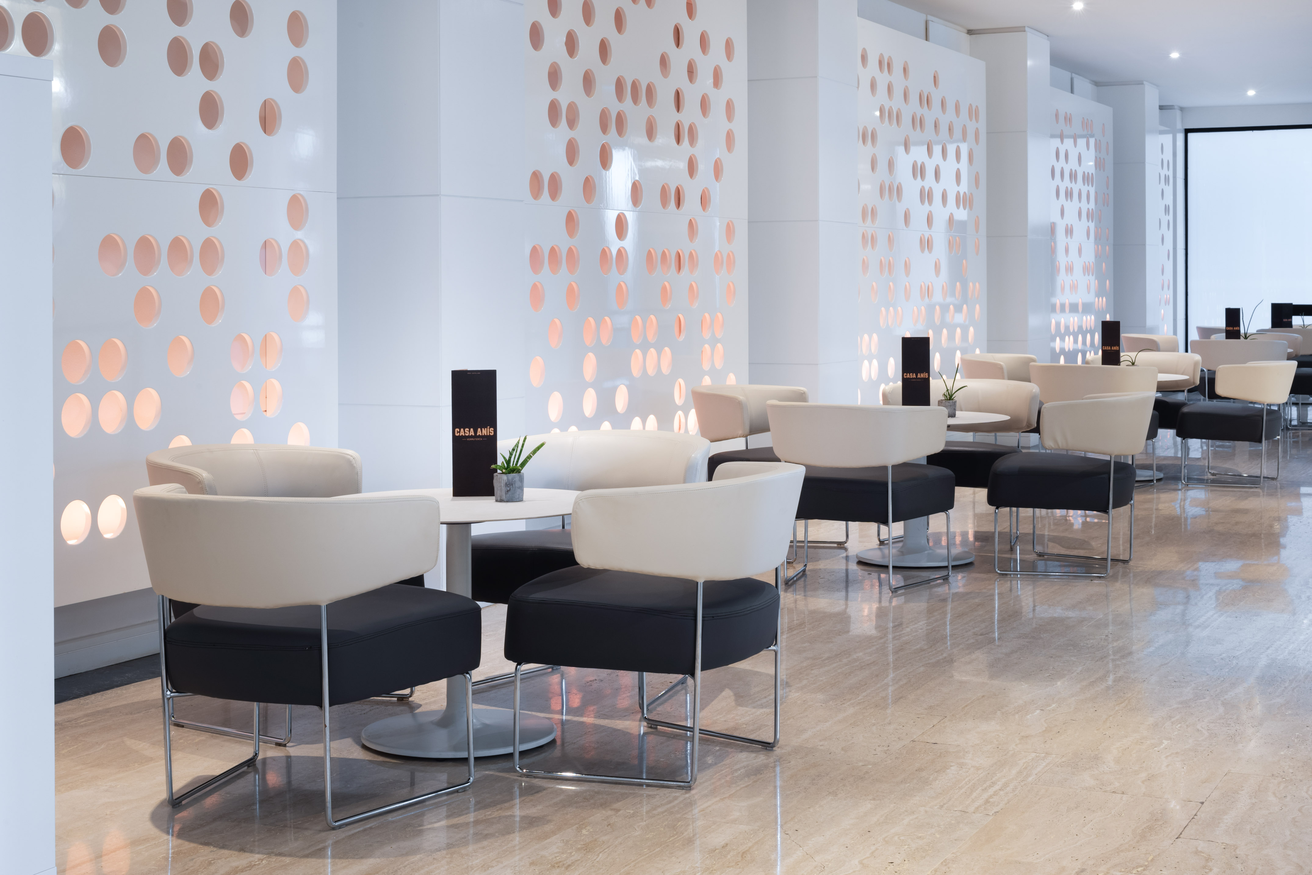 Modern cafe lounge with white perforated walls, cream and black seating.