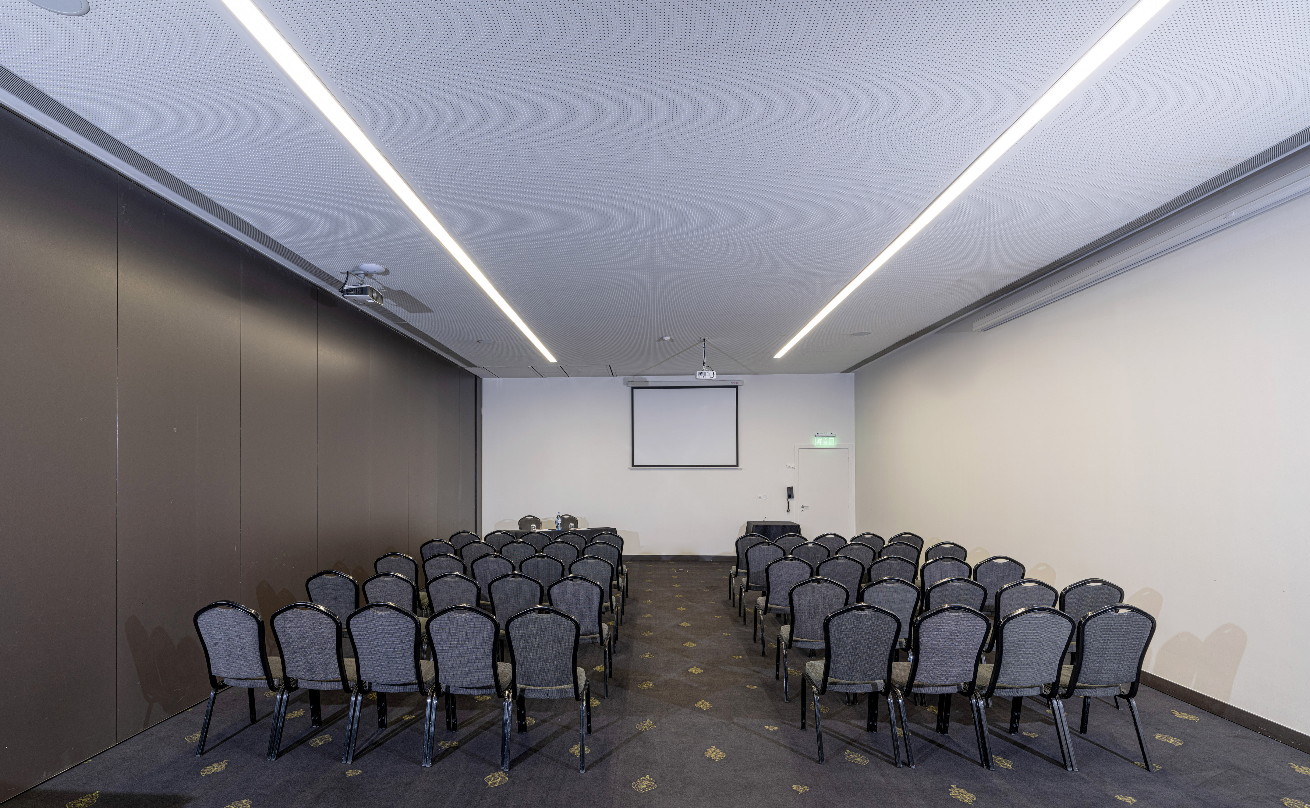 Empty conference room with rows of gray chairs, a projector, and screen.