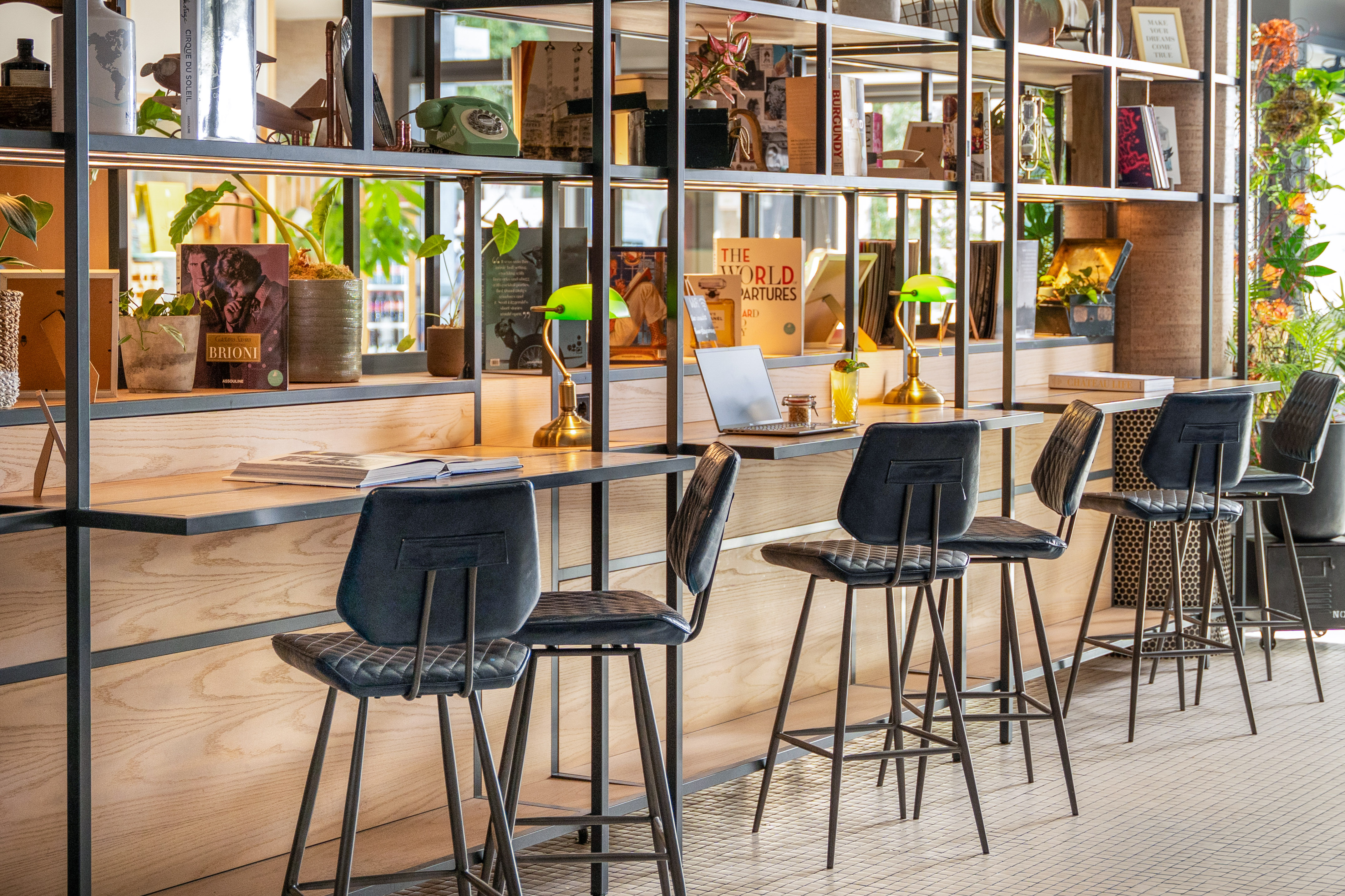 Stylish library lounge with work desks, plants, books, and modern bar stools.