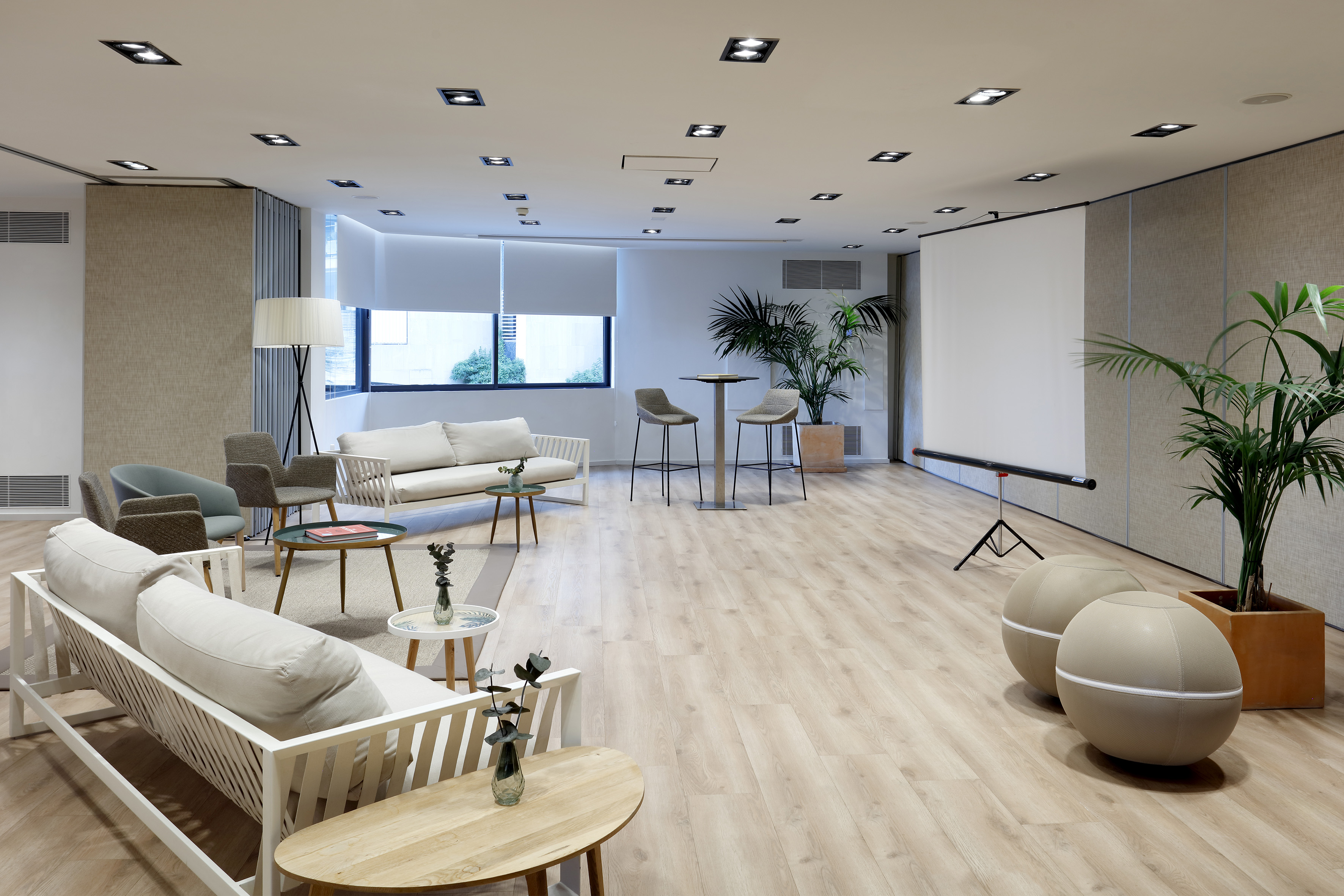 Contemporary lounge with diverse seating, projector screen, and wood floor.