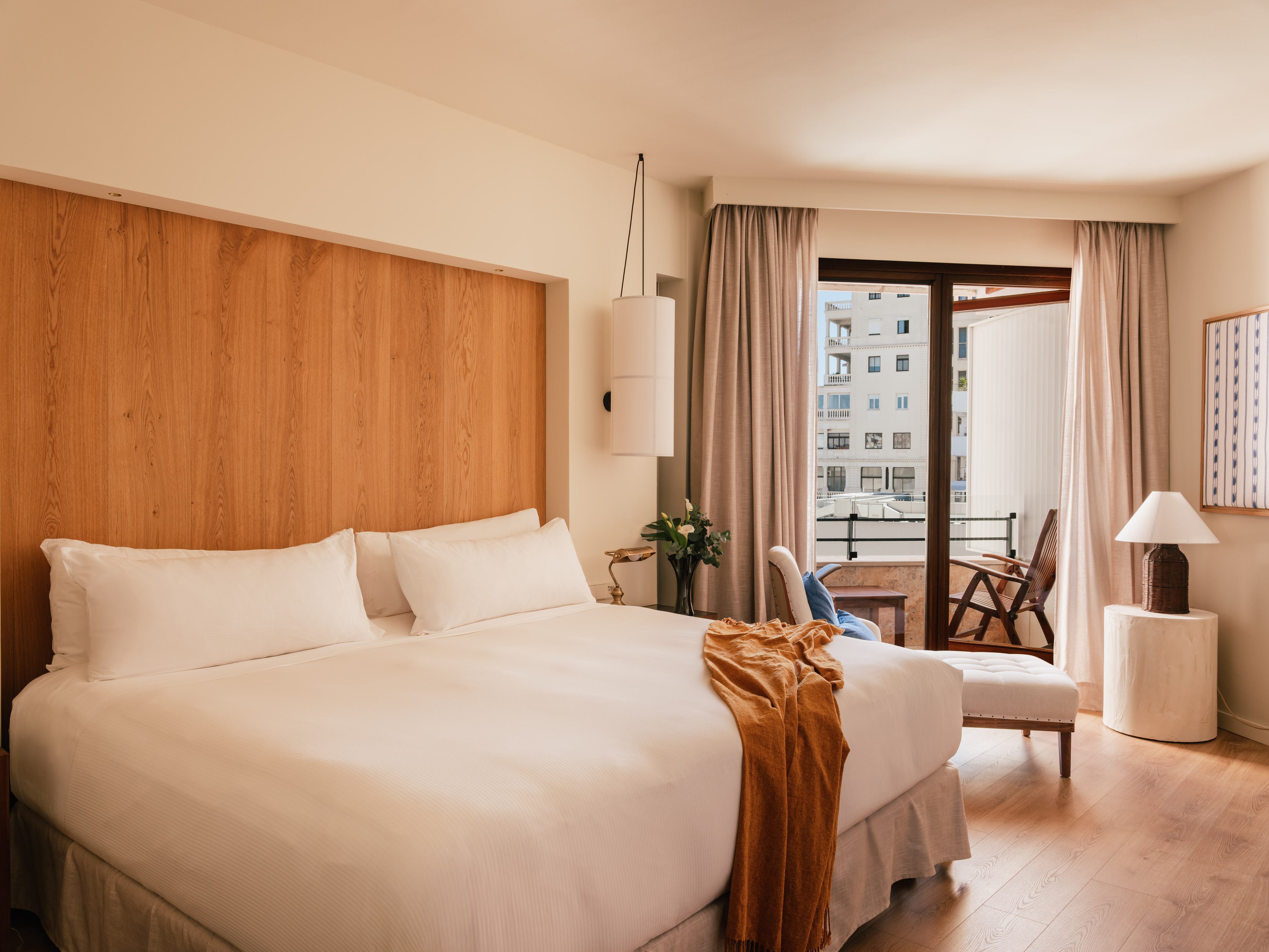 Modern hotel room with wood headboard, large bed, and balcony city view.
