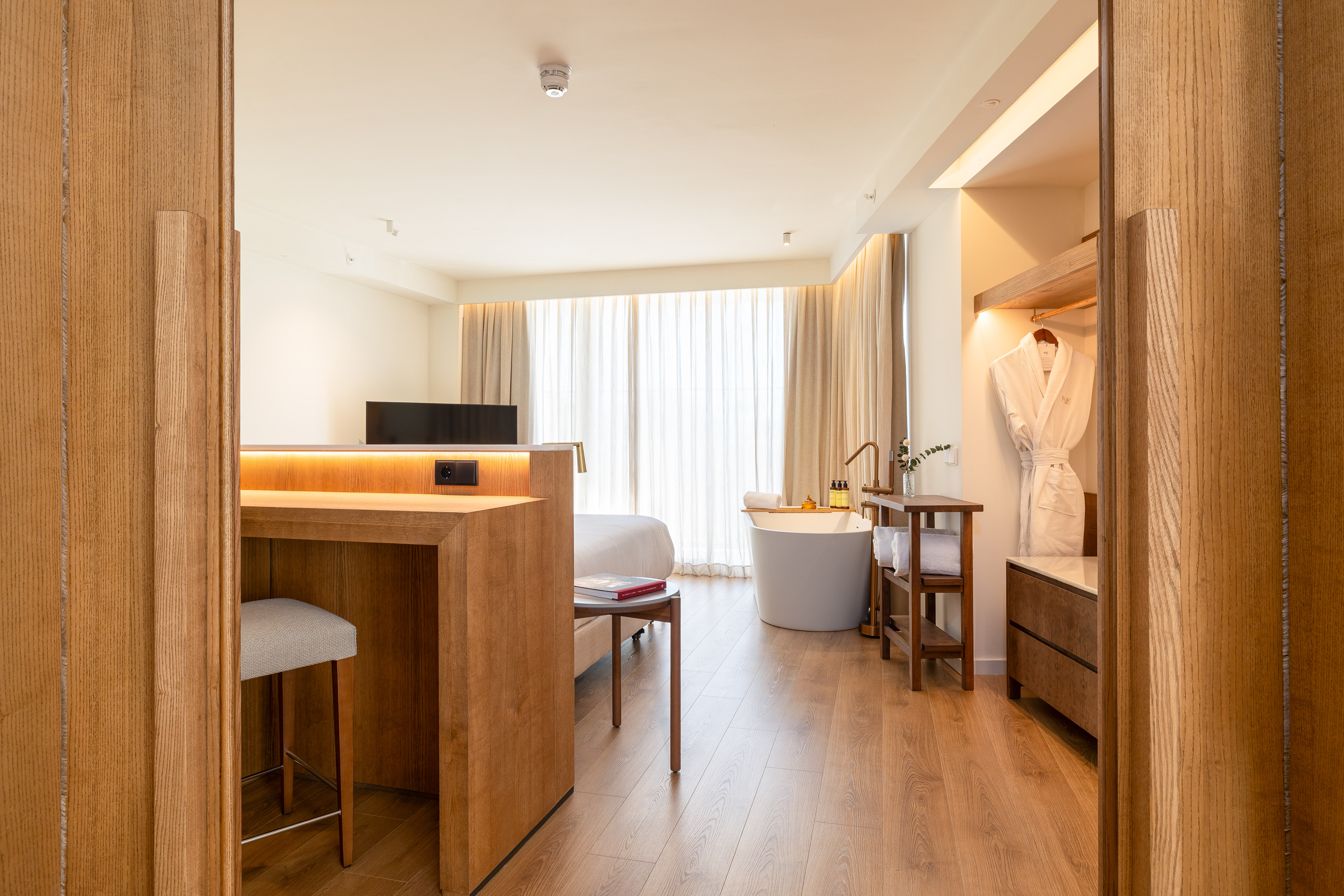 Modern luxury hotel room with freestanding tub, wooden floor, and desk area.