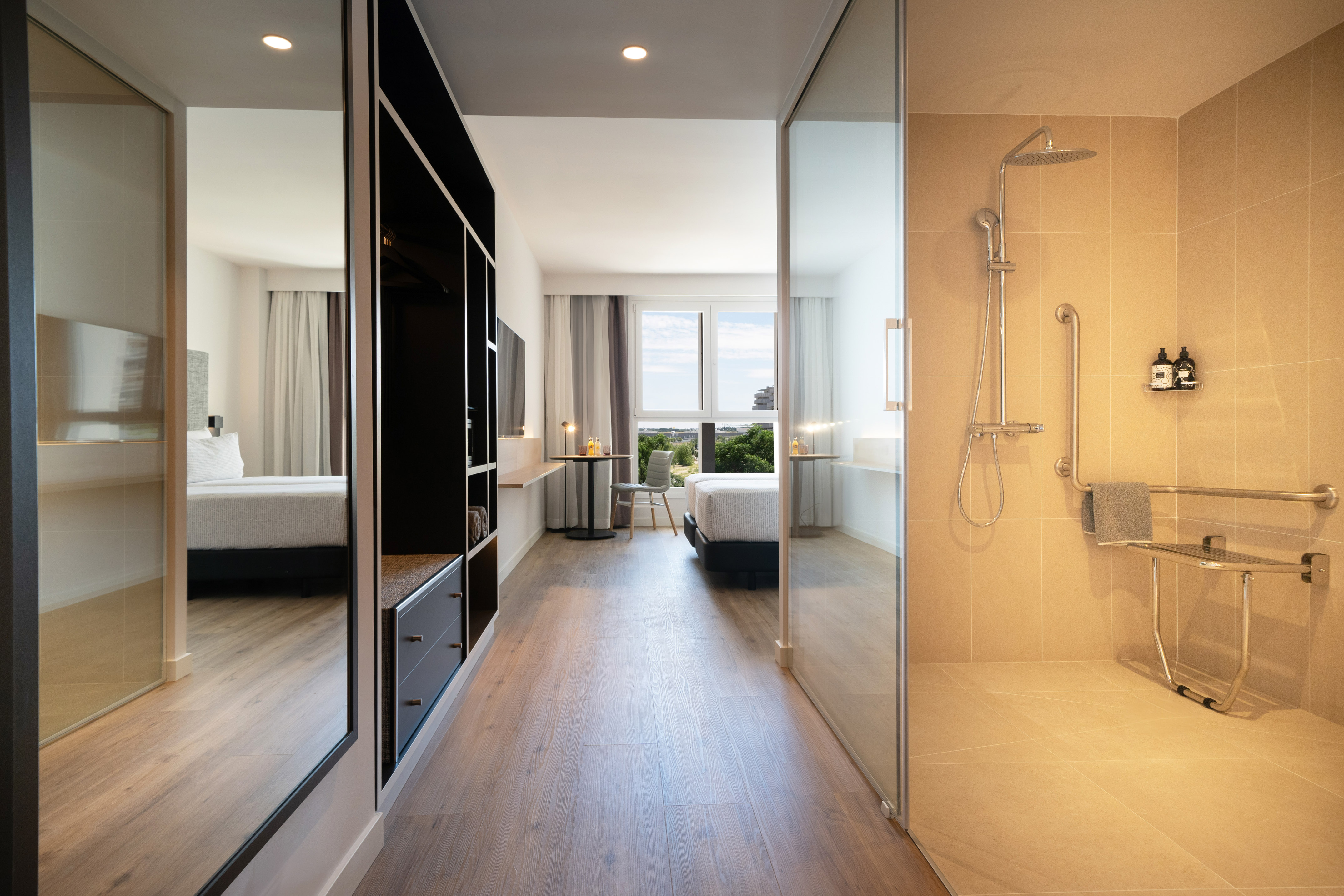 Modern hotel room with bed, wardrobe, and accessible walk-in shower.