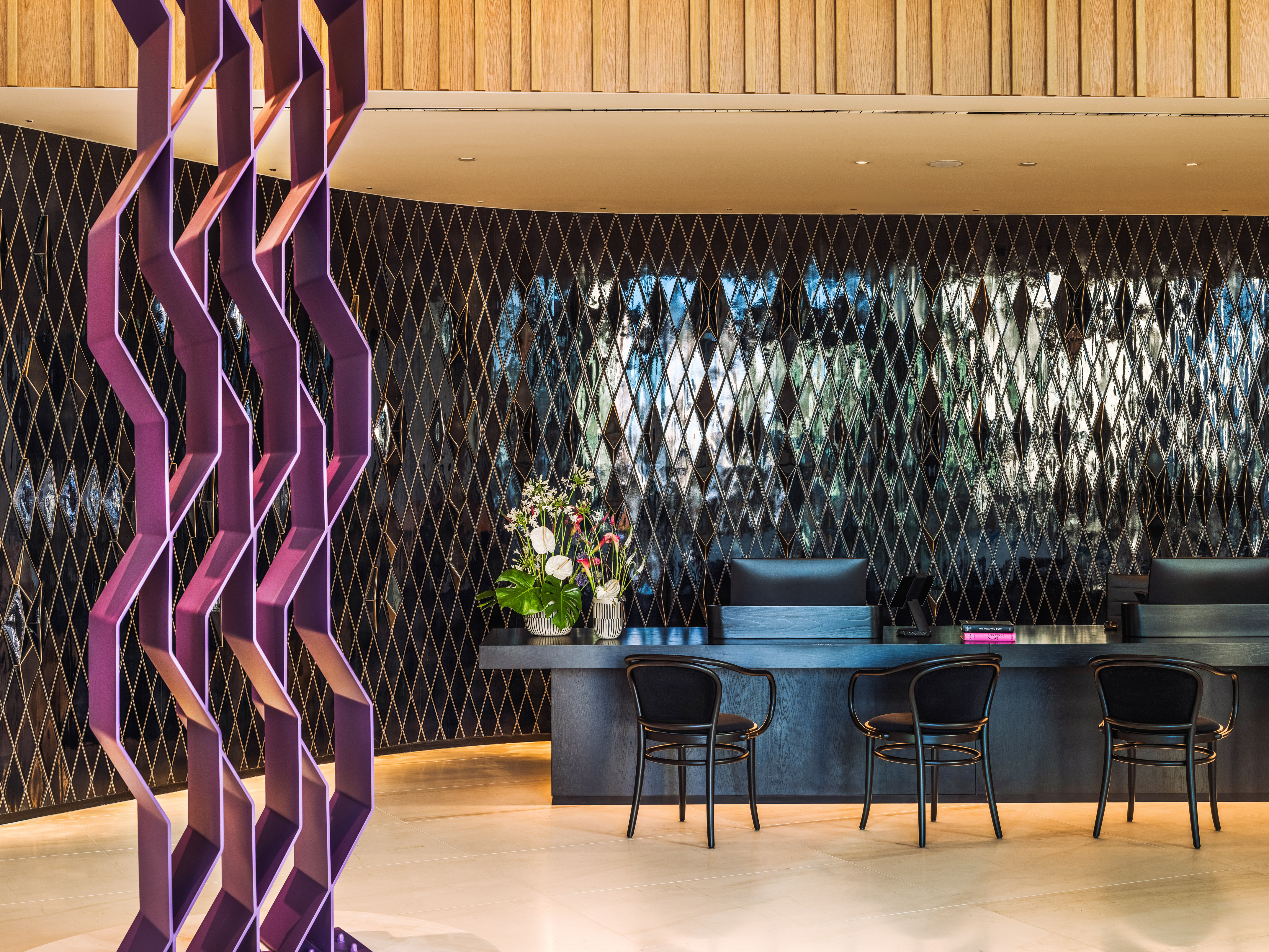 Modern hotel lobby featuring dark reception desk, patterned wall, and purple art.