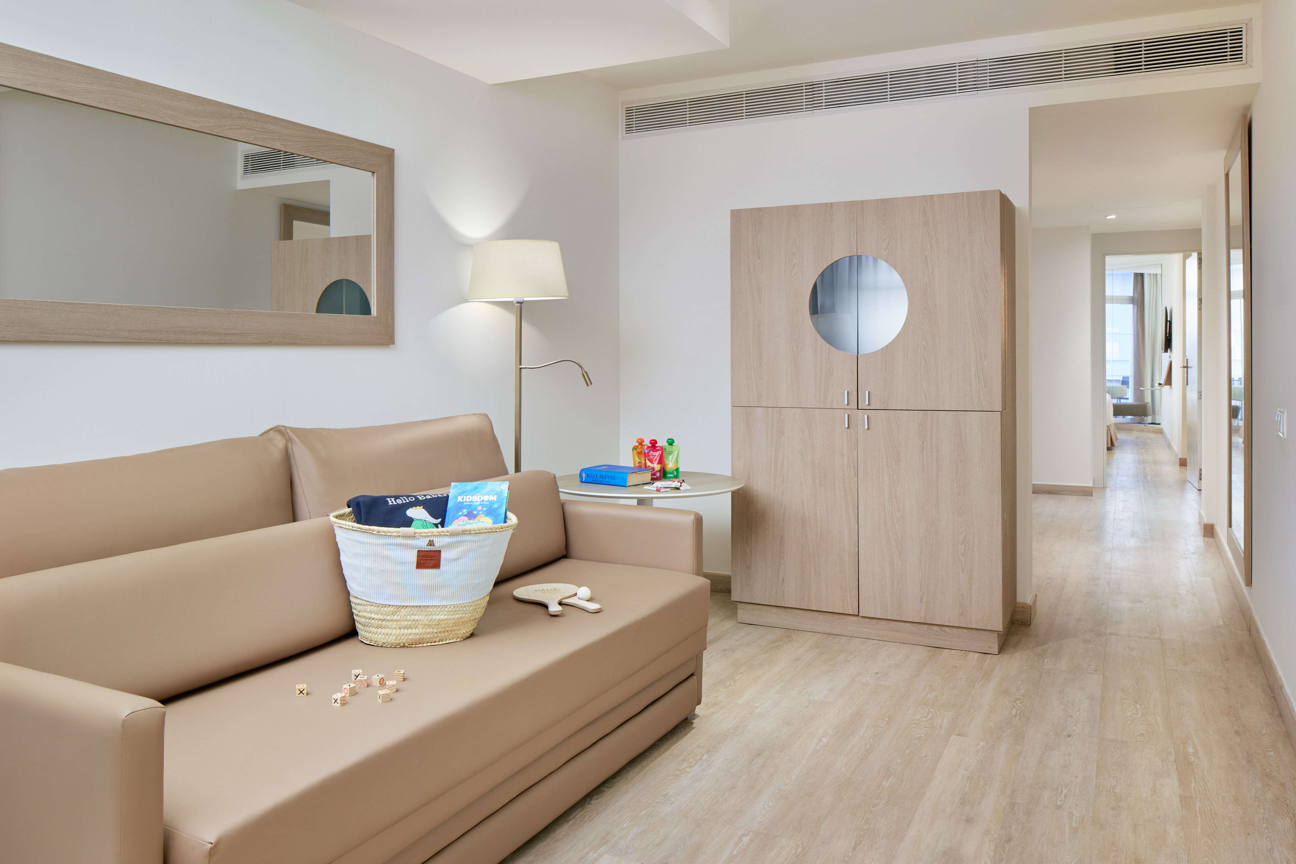 Family suite lounge with tan sofa, kids' activity basket, and modern wood furniture.