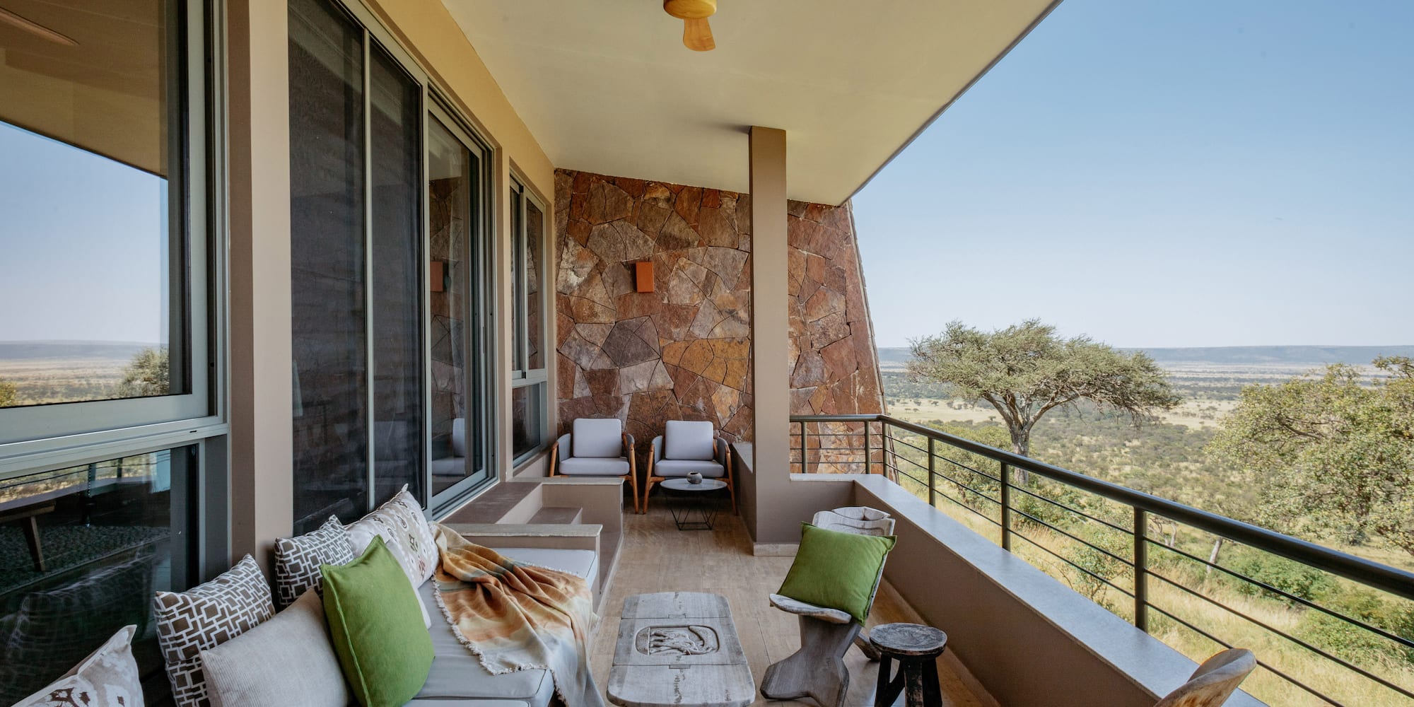 Balcony at safari lodge with outdoor sofa, stone wall, and savanna landscape.