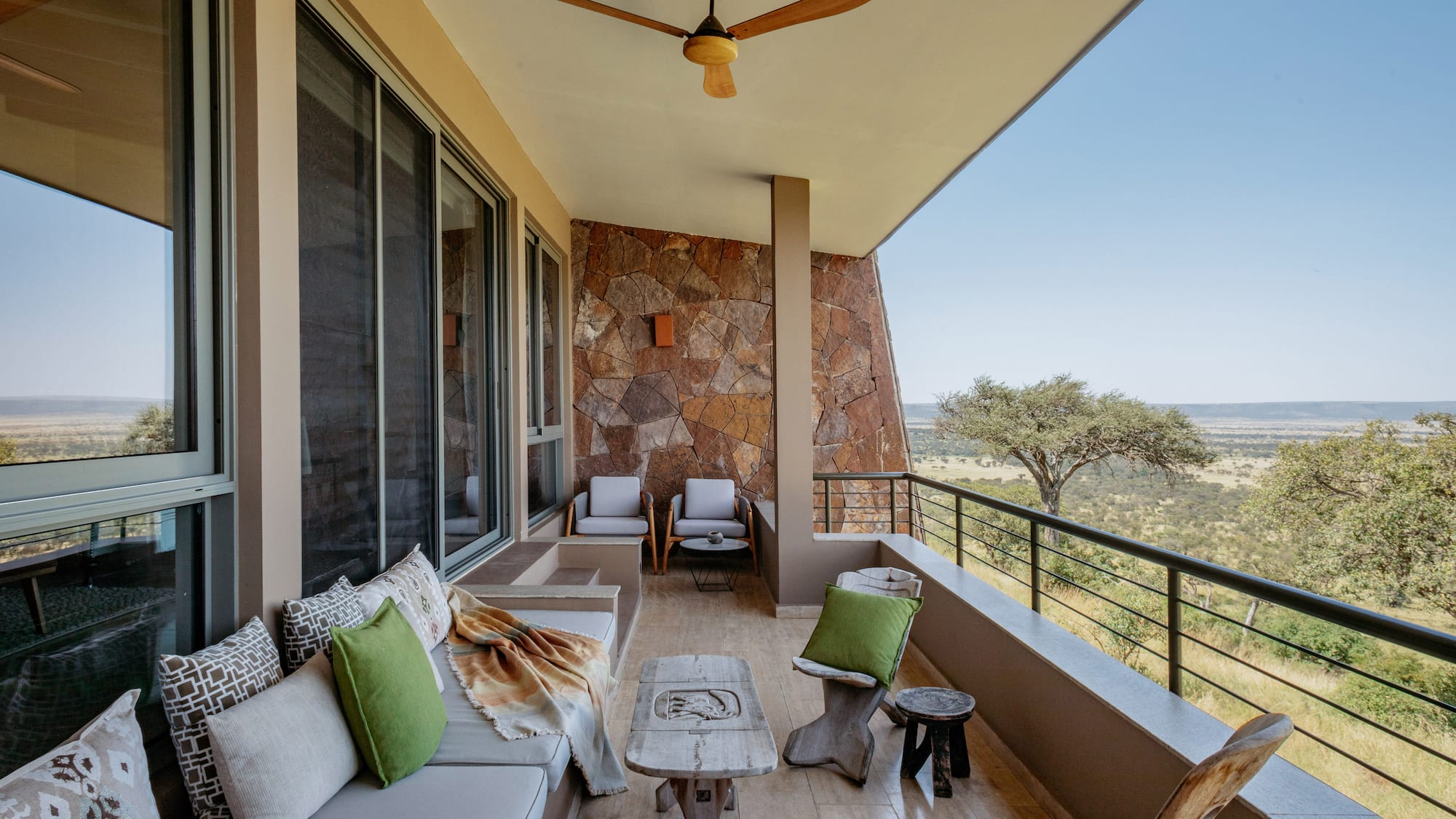 Balcony at safari lodge with outdoor sofa, stone wall, and savanna landscape.