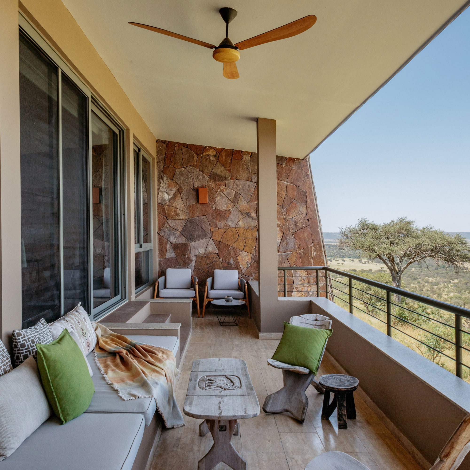 Balcony at safari lodge with outdoor sofa, stone wall, and savanna landscape.