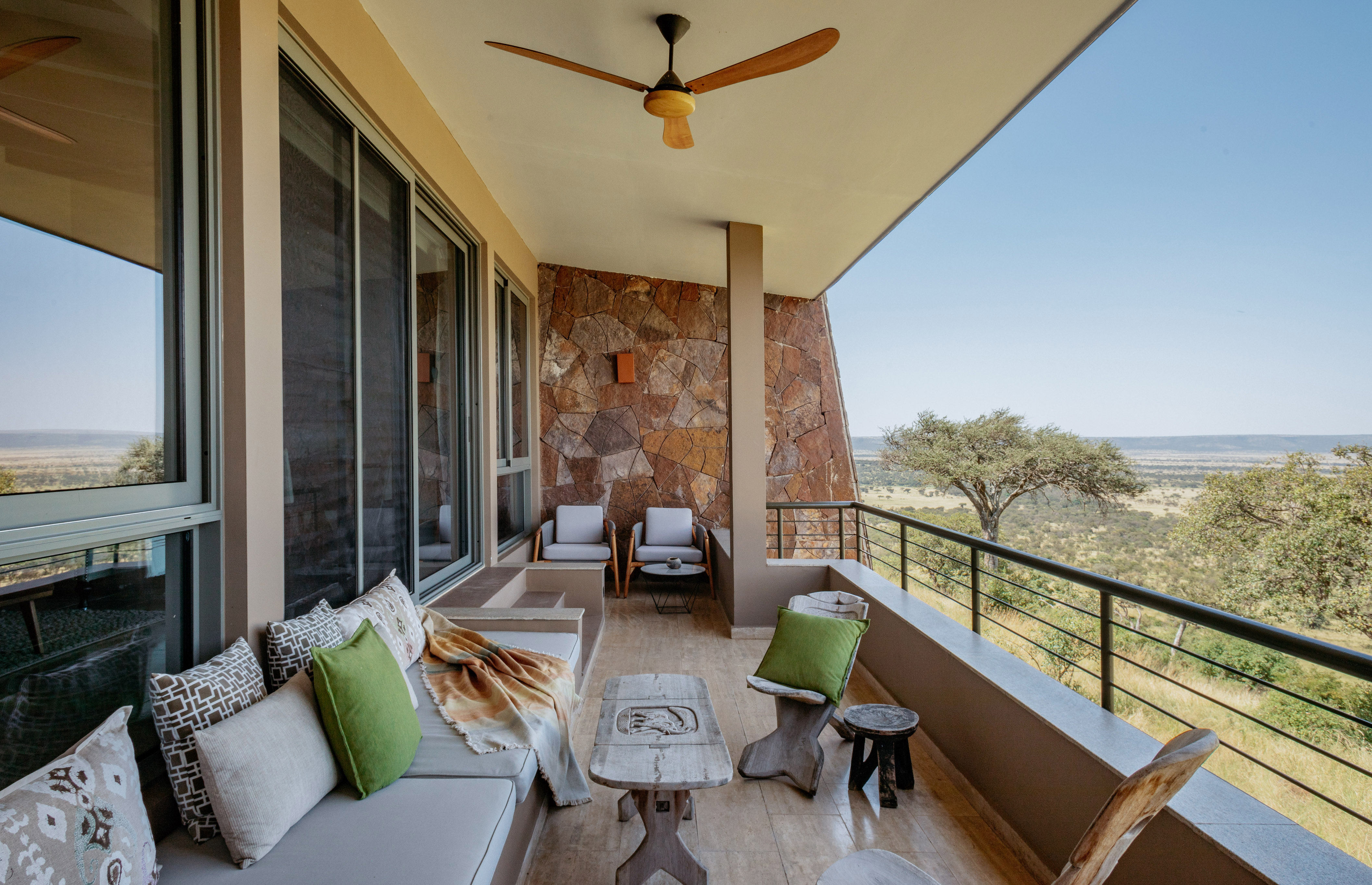 Balcony at safari lodge with outdoor sofa, stone wall, and savanna landscape.