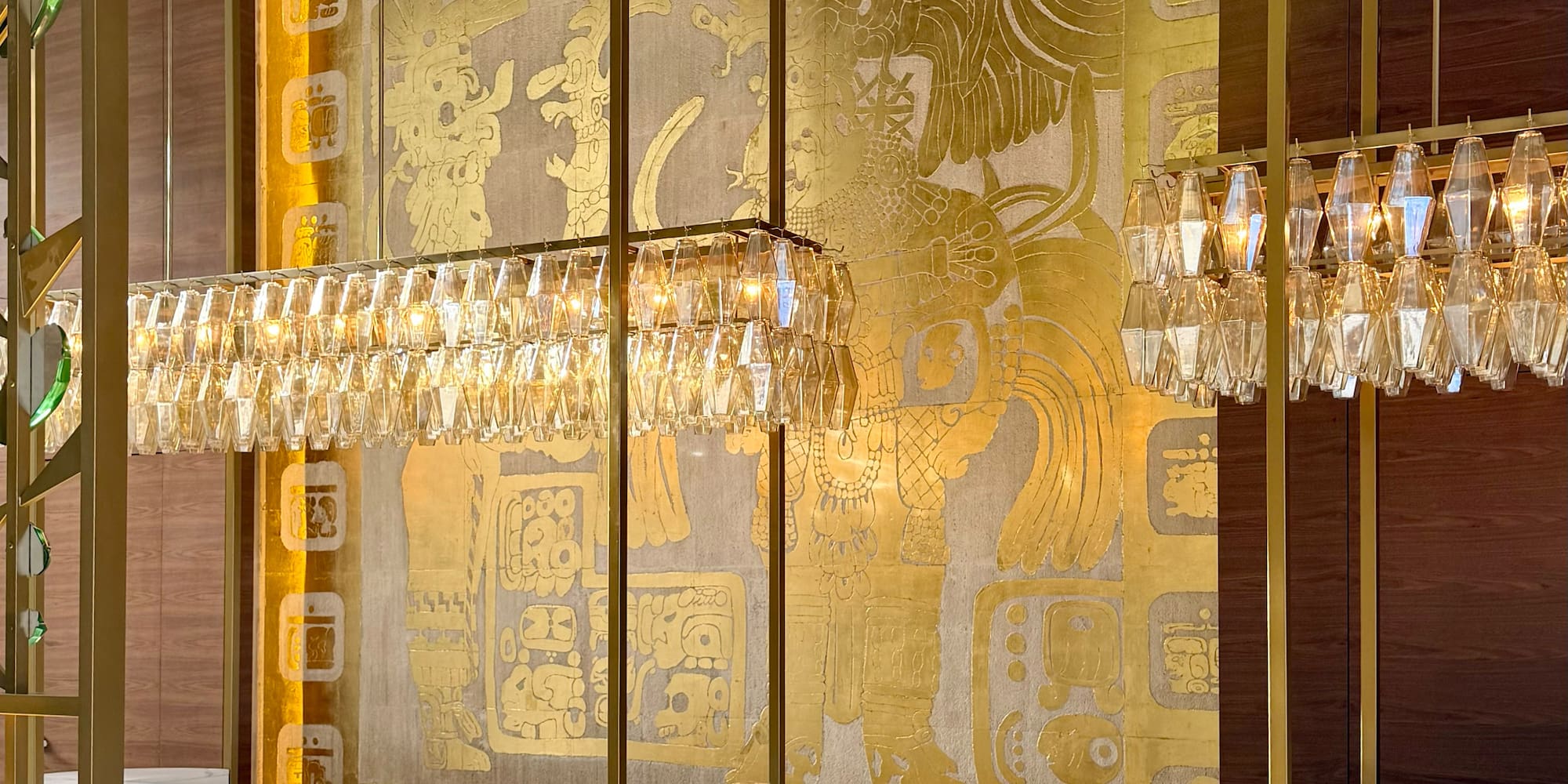 Luxury hotel lobby: marble reception, crystal chandeliers, gold Mayan mural.