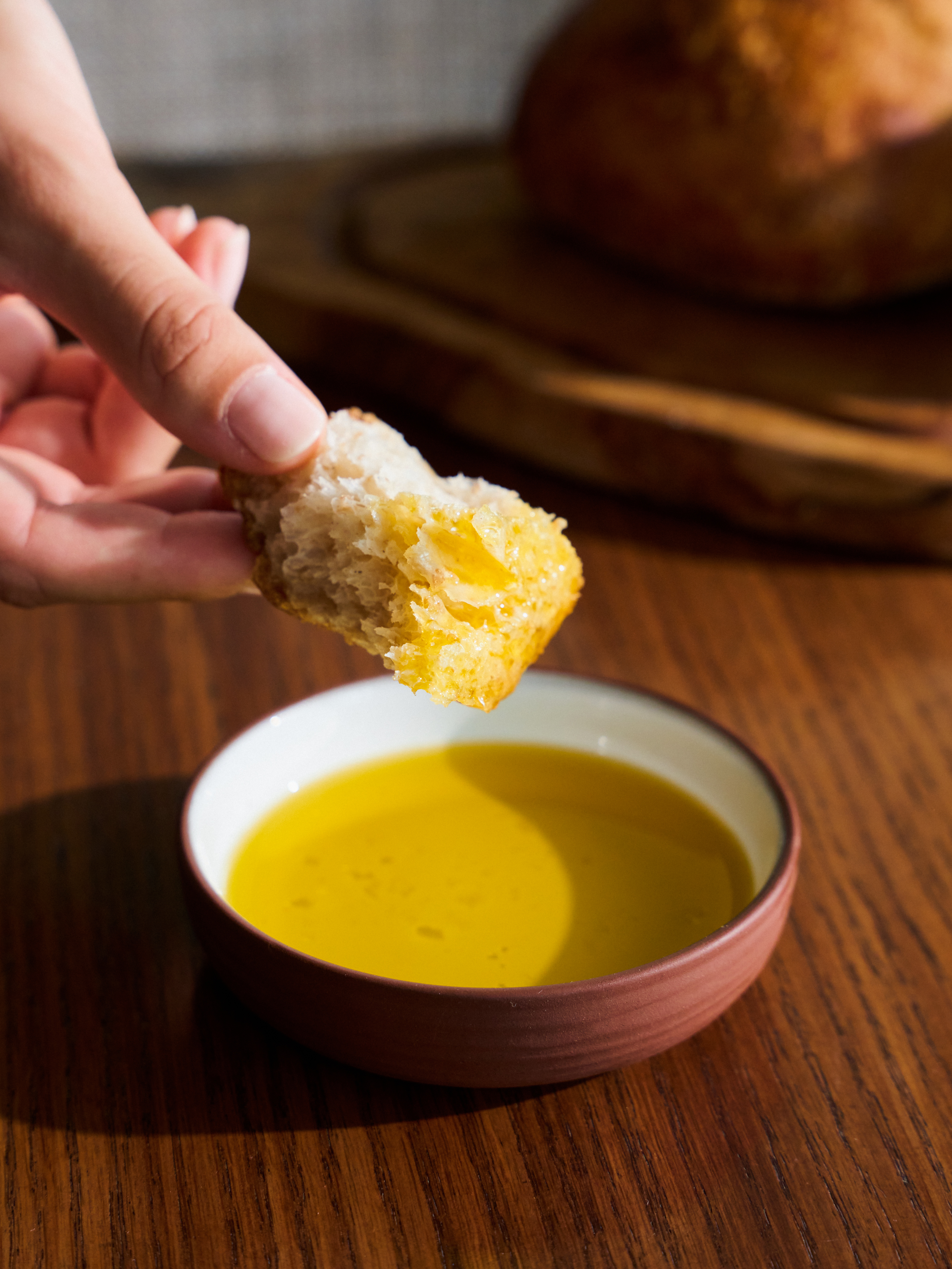 Hand dipping rustic bread into extra virgin olive oil.