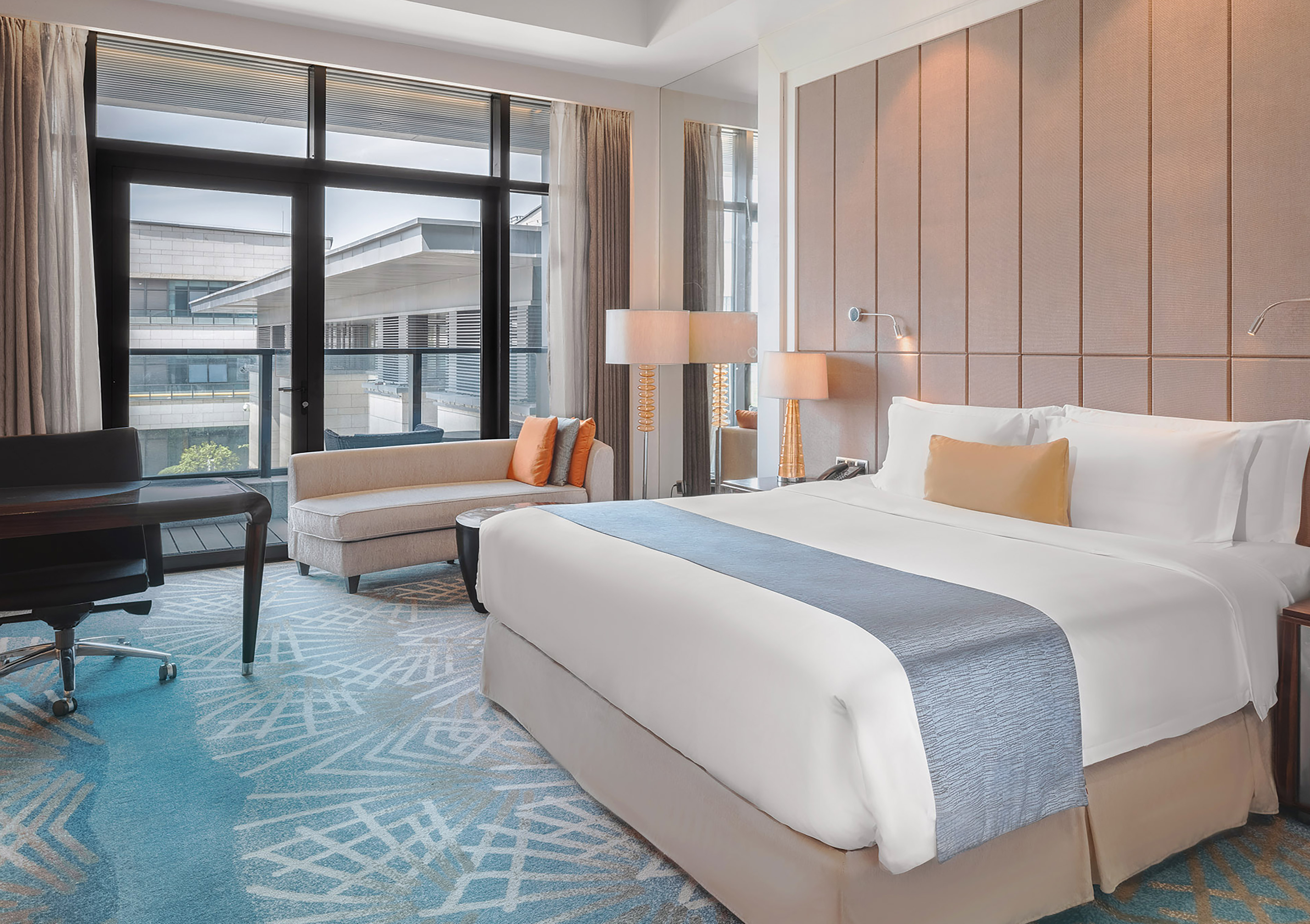 Modern hotel suite with king bed, work desk, and large windows.