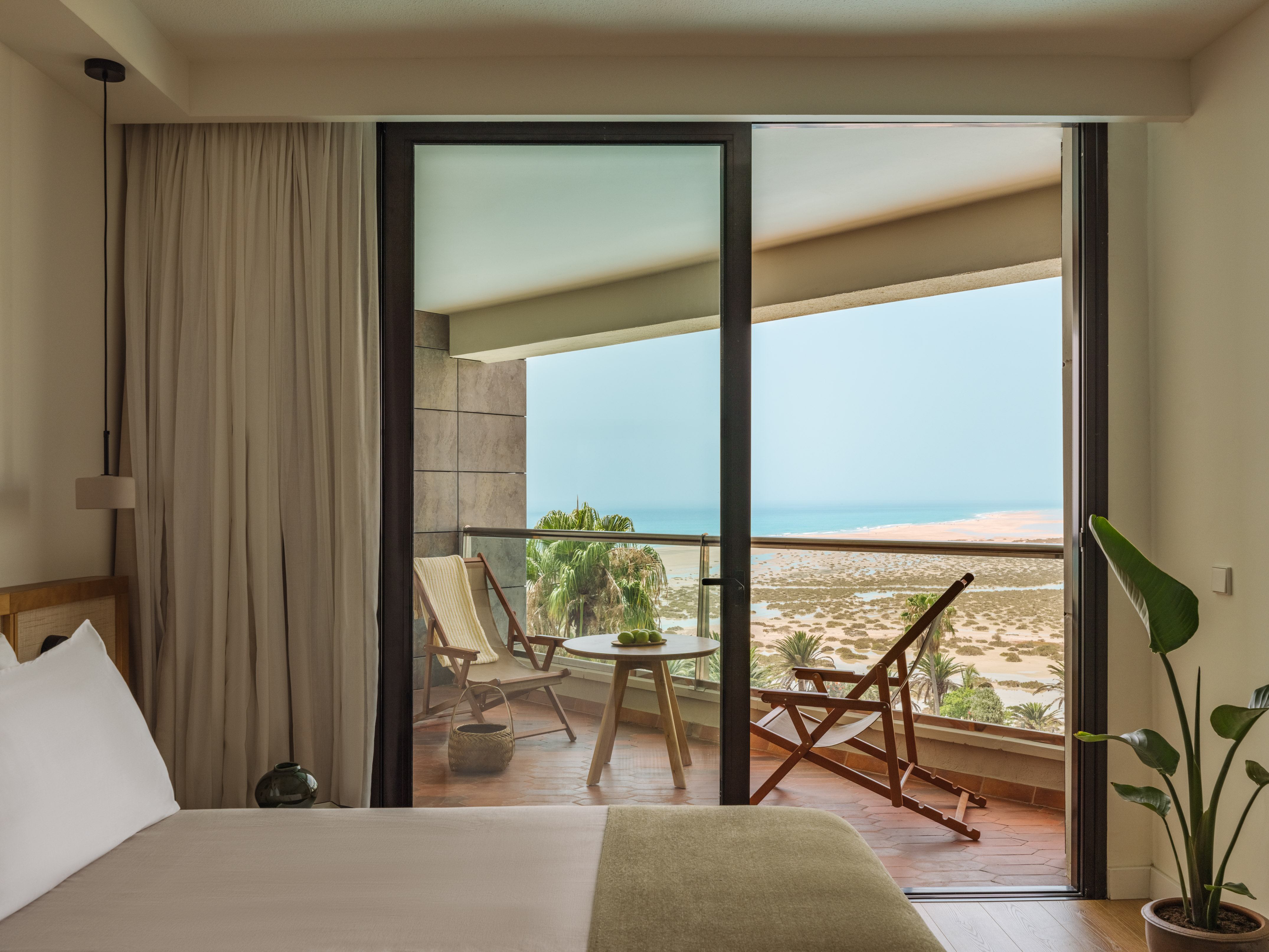 Hotel room balcony with ocean, beach, and desert landscape view.