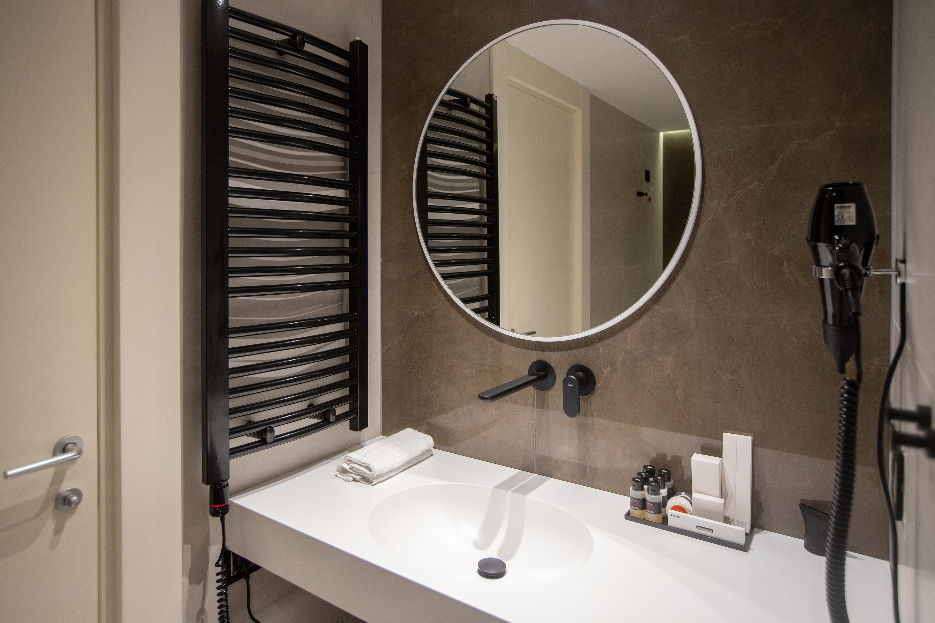 Modern bathroom vanity with white sink, round mirror, black towel warmer.