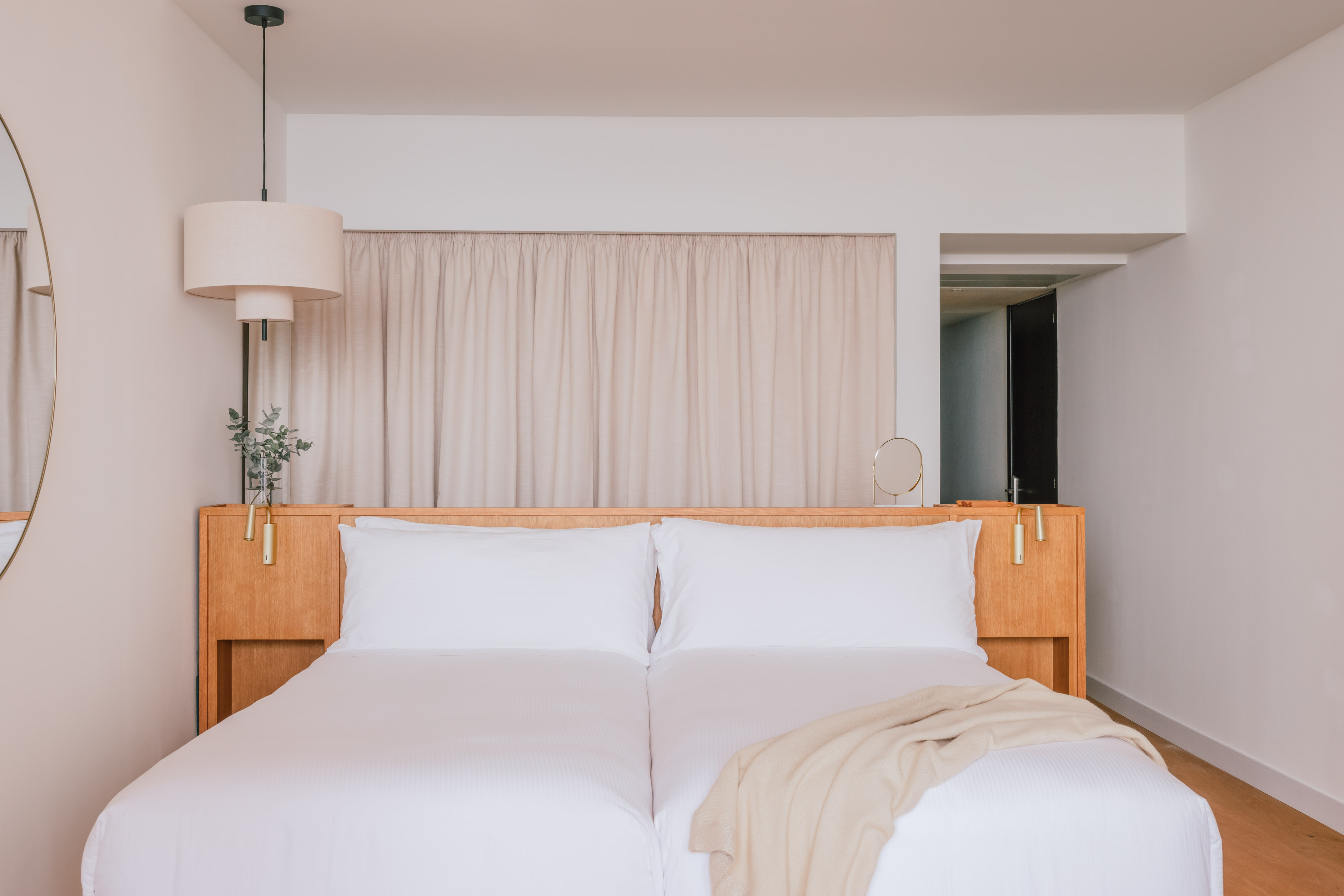 Modern hotel bedroom with wooden headboard, twin beds, and neutral decor.