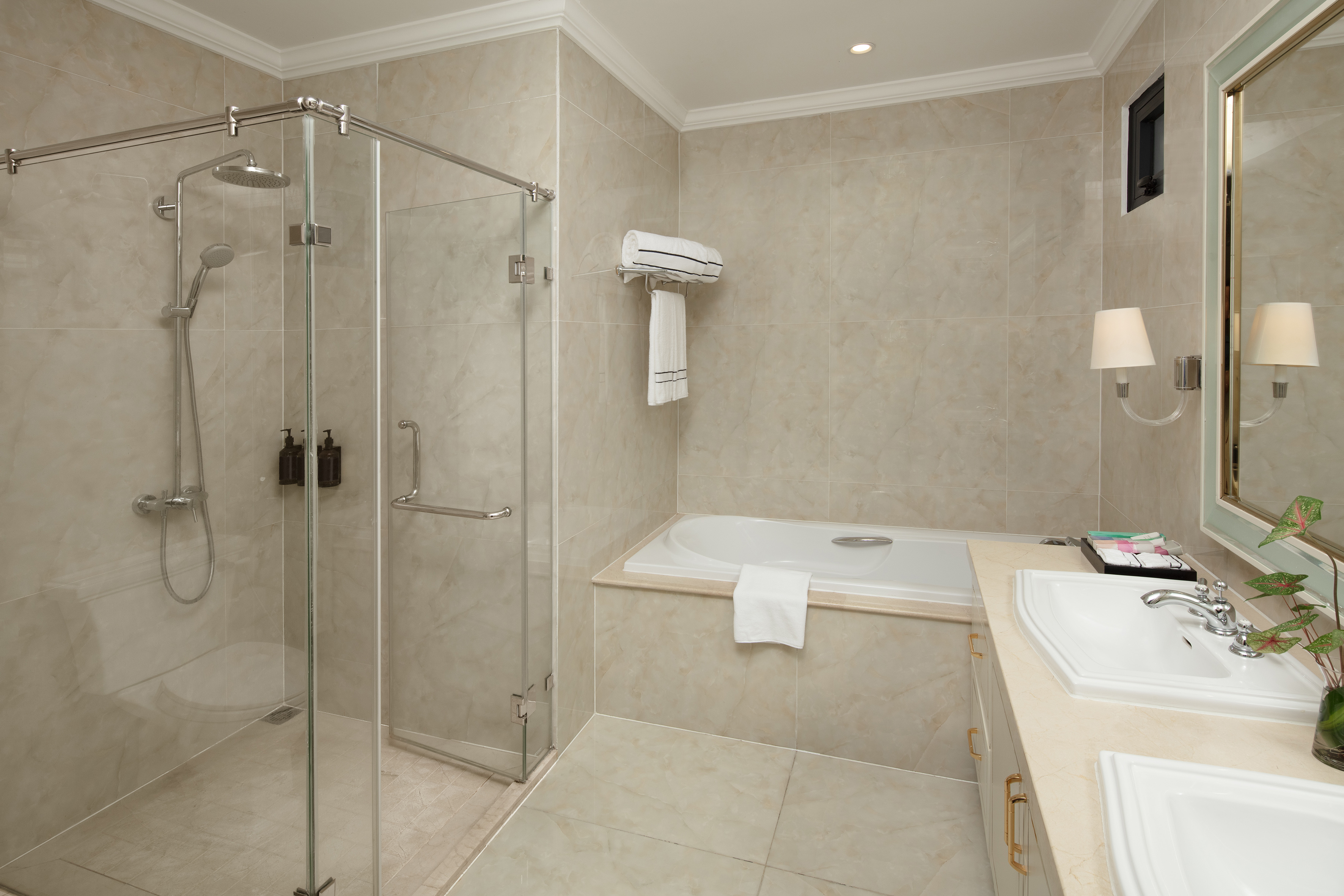 Tiled bathroom with glass shower, built-in tub, and double sink vanity.