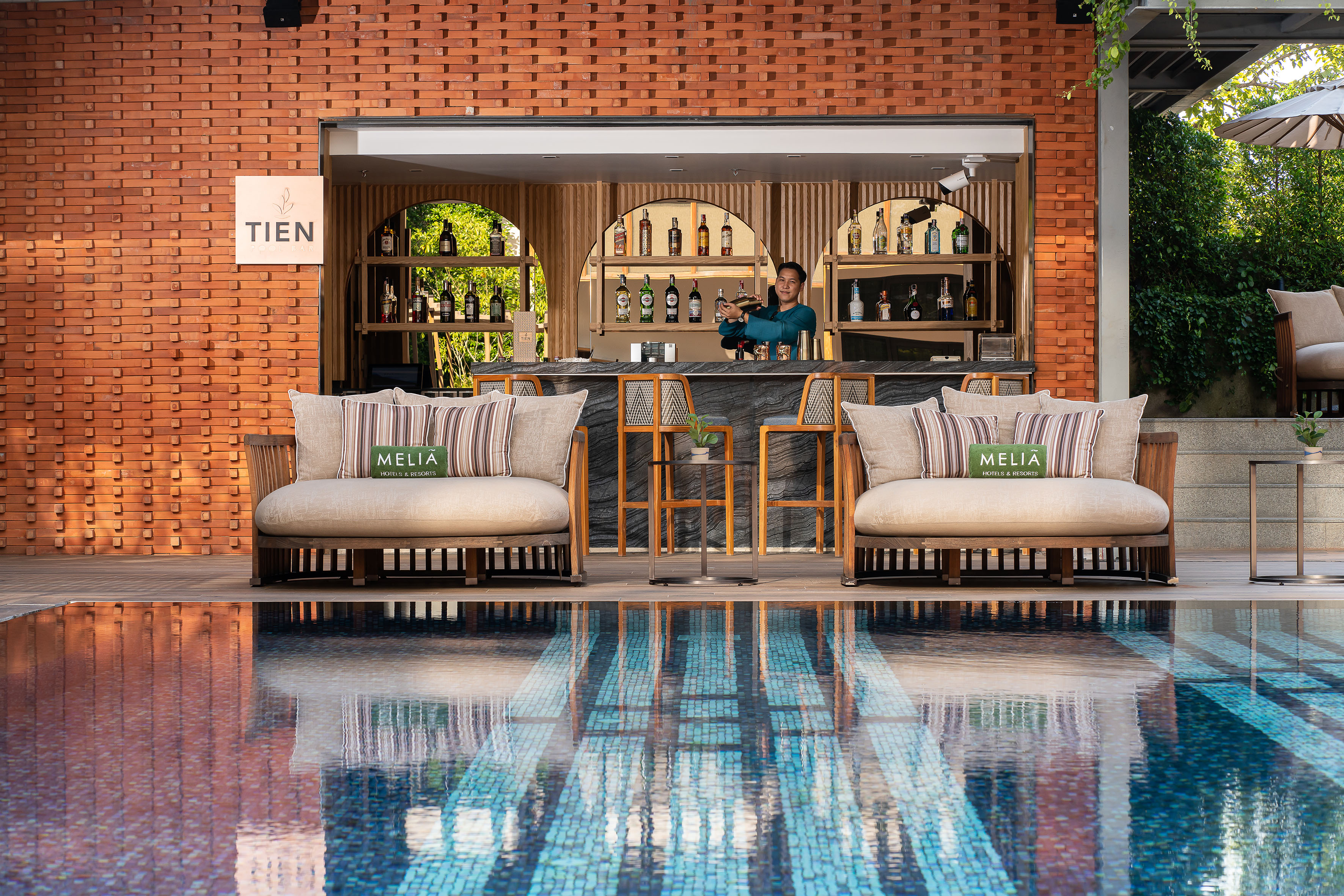 Melia resort poolside bar with bartender, lounge seating, and reflecting pool.