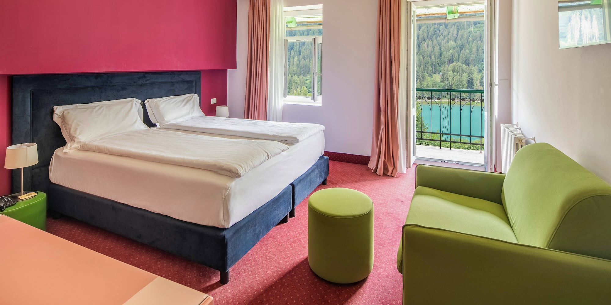 Hotel room with balcony lake view, double bed, red wall, green sofa.