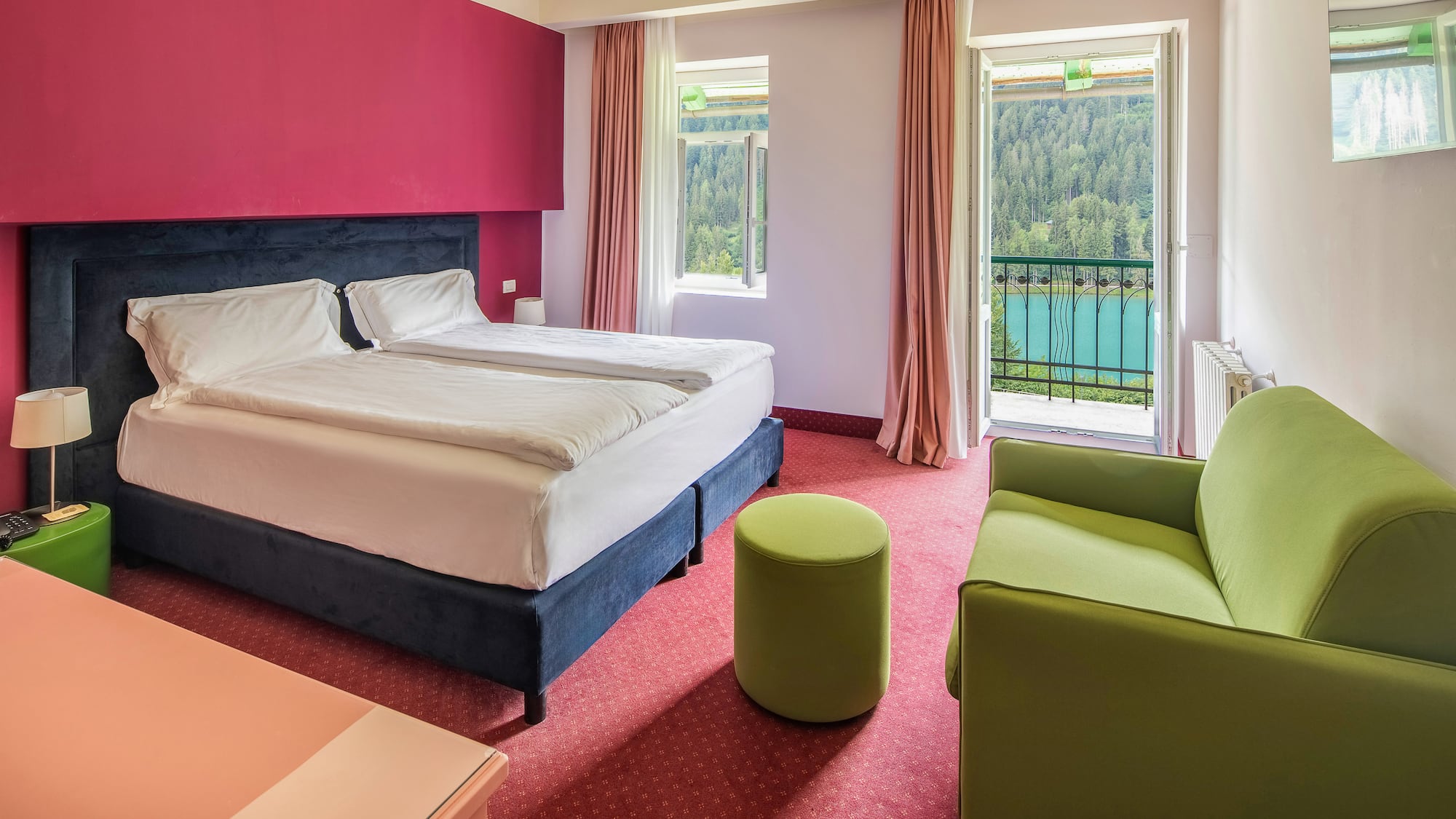 Hotel room with balcony lake view, double bed, red wall, green sofa.