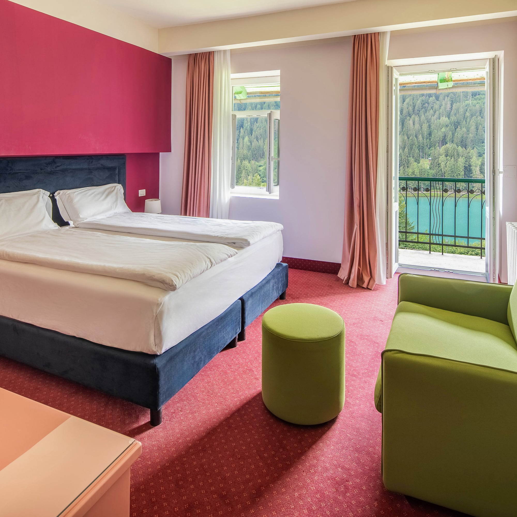 Hotel room with balcony lake view, double bed, red wall, green sofa.