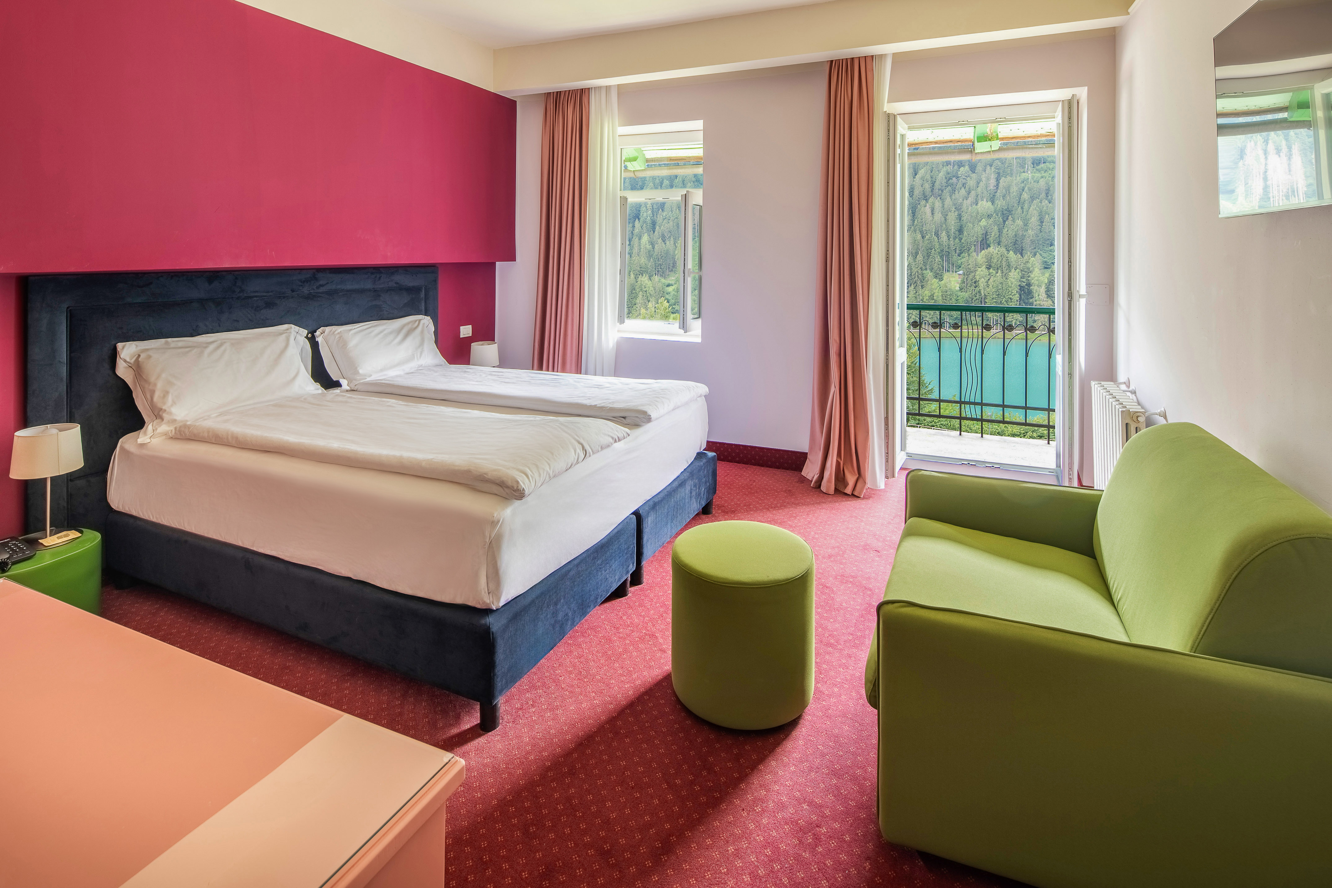 Hotel room with balcony lake view, double bed, red wall, green sofa.