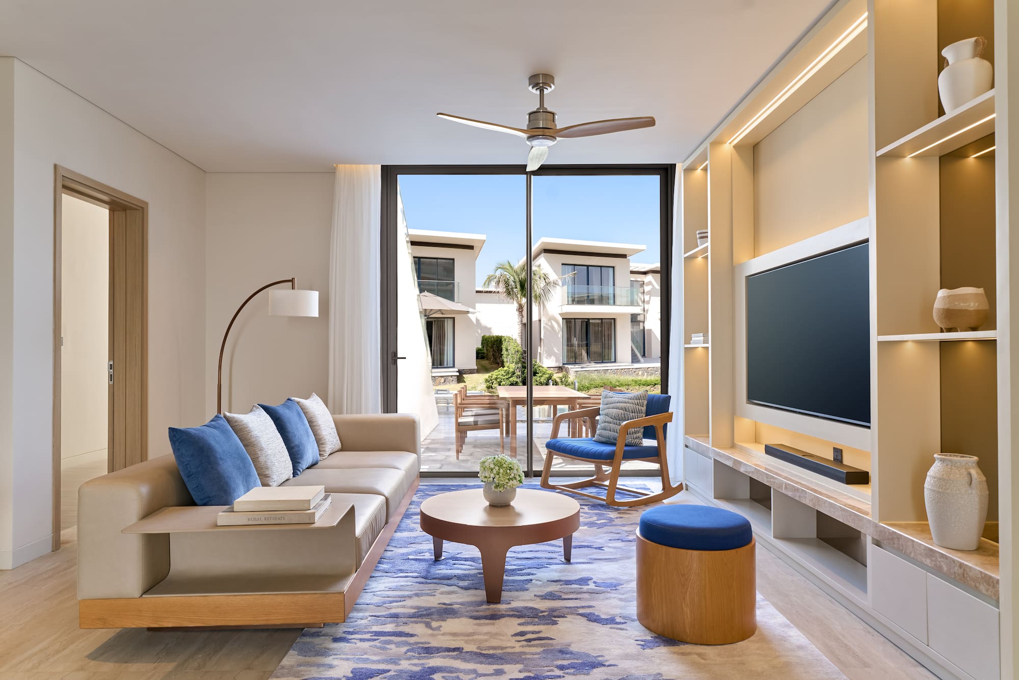 Luxury modern living room with beige sofa, blue rug, and outdoor villa view.