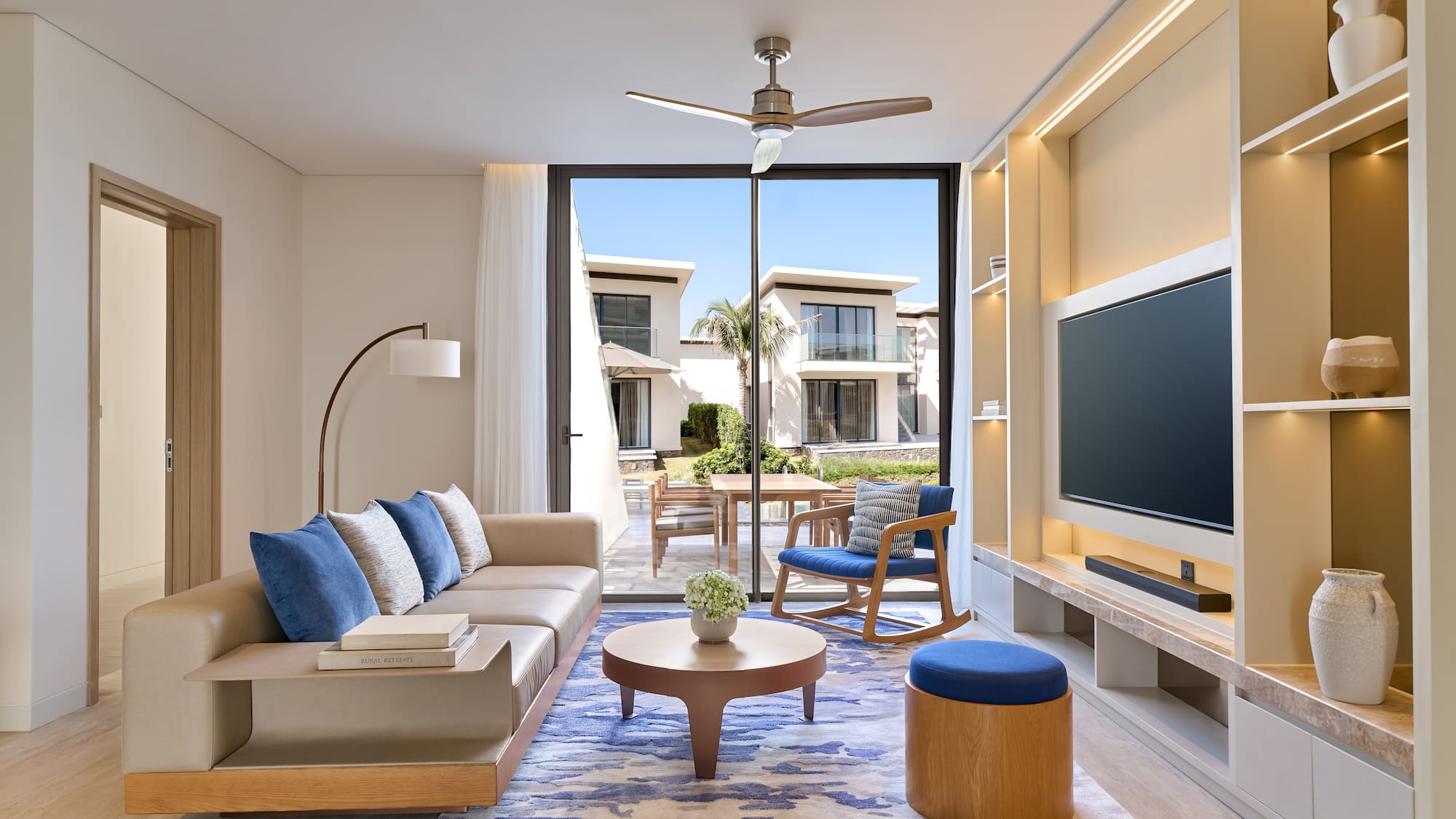 Luxury modern living room with beige sofa, blue rug, and outdoor villa view.