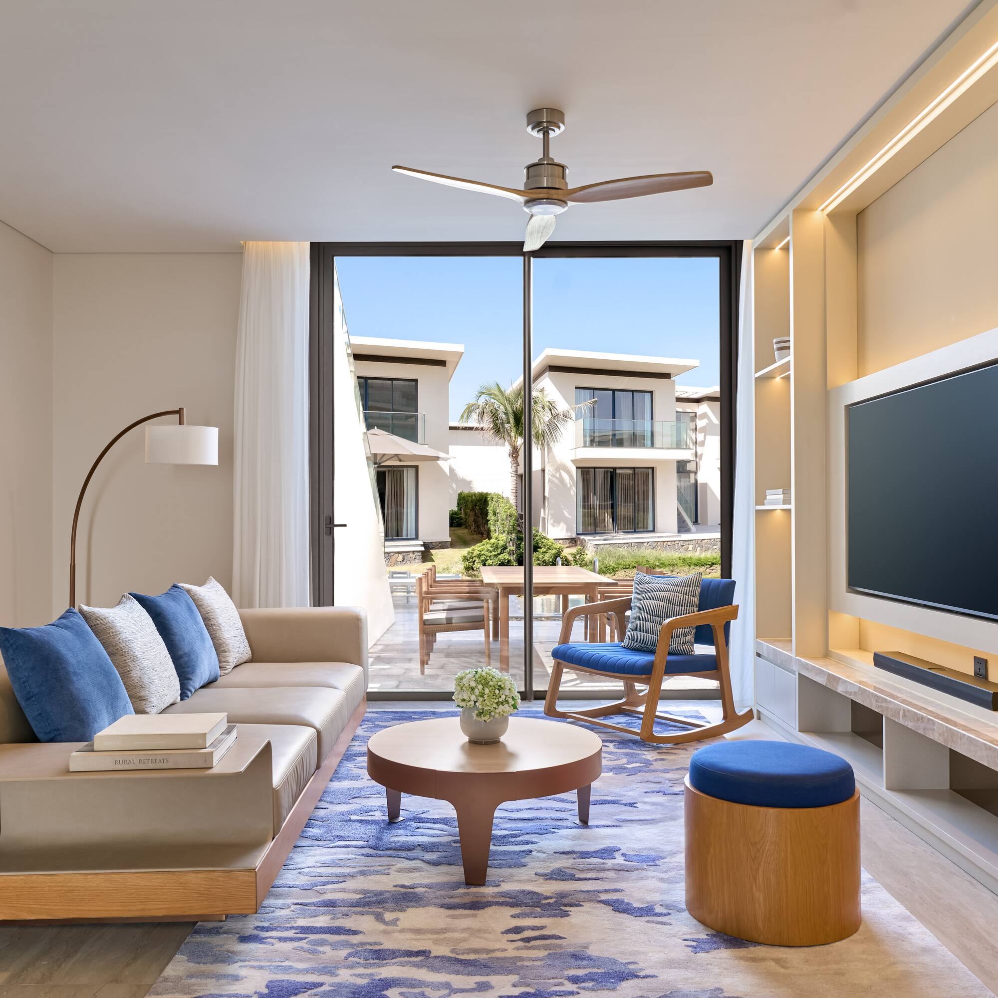 Luxury modern living room with beige sofa, blue rug, and outdoor villa view.