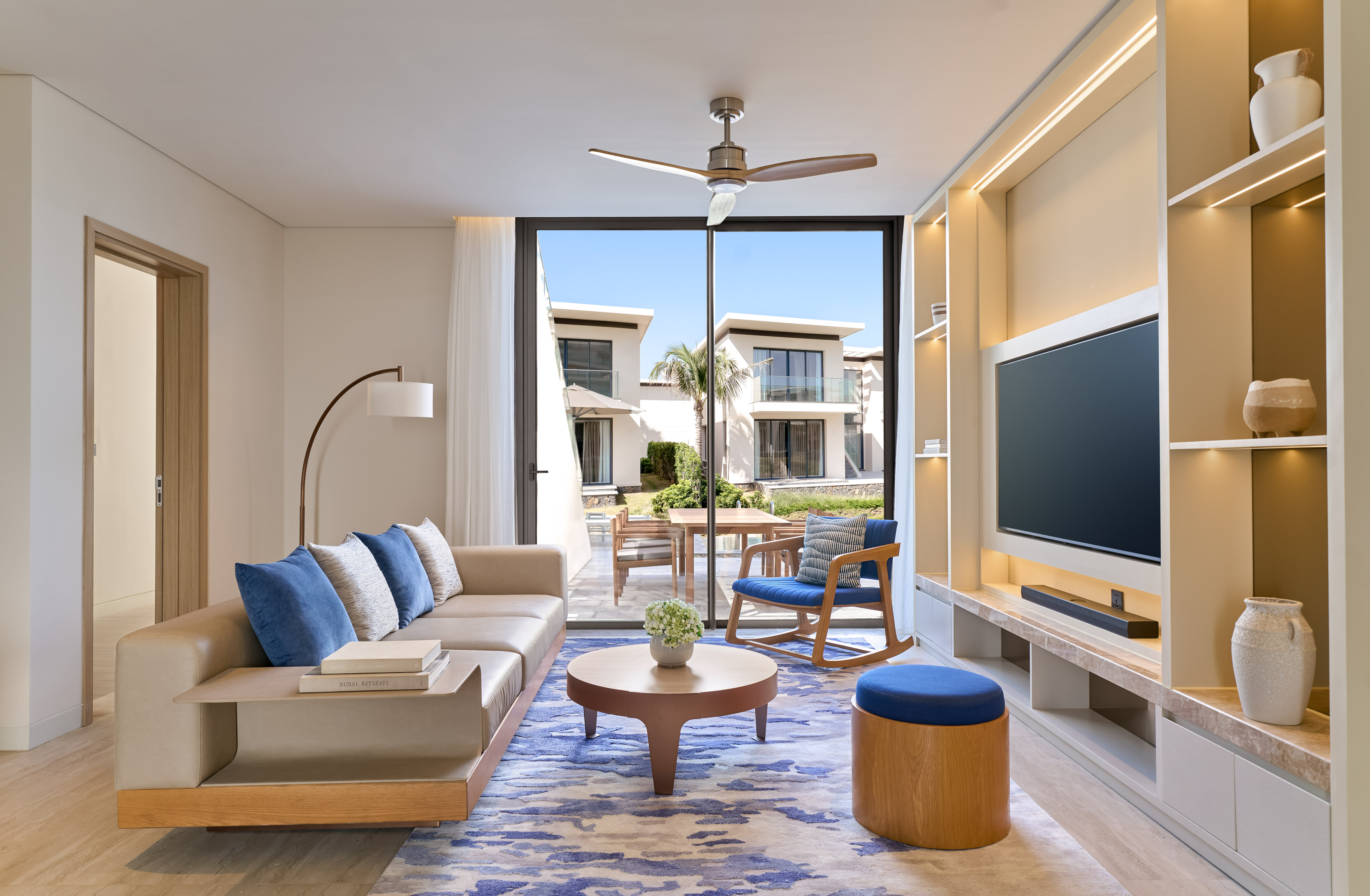 Luxury modern living room with beige sofa, blue rug, and outdoor villa view.