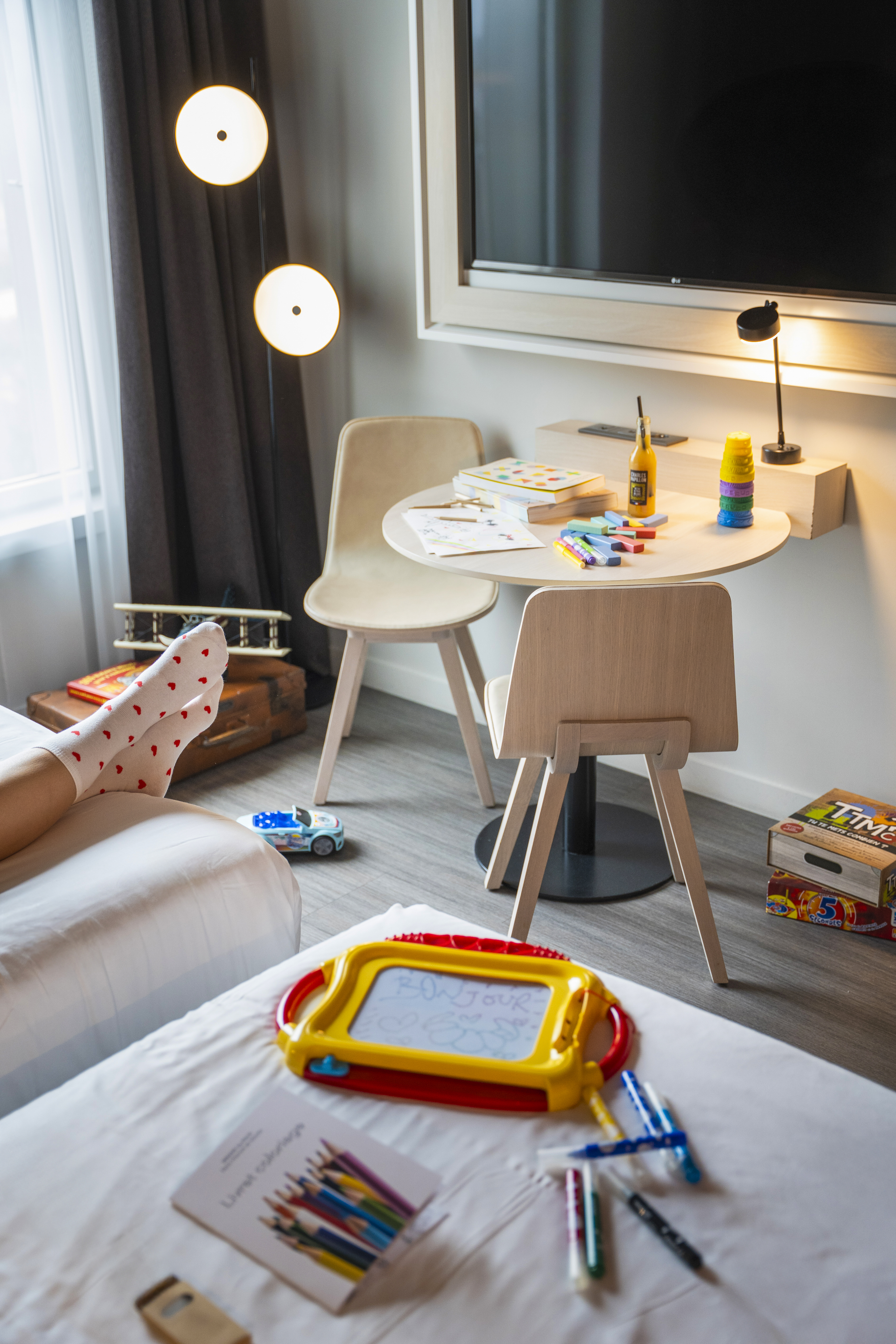 a child's feet on a bed in a room with a table and toys