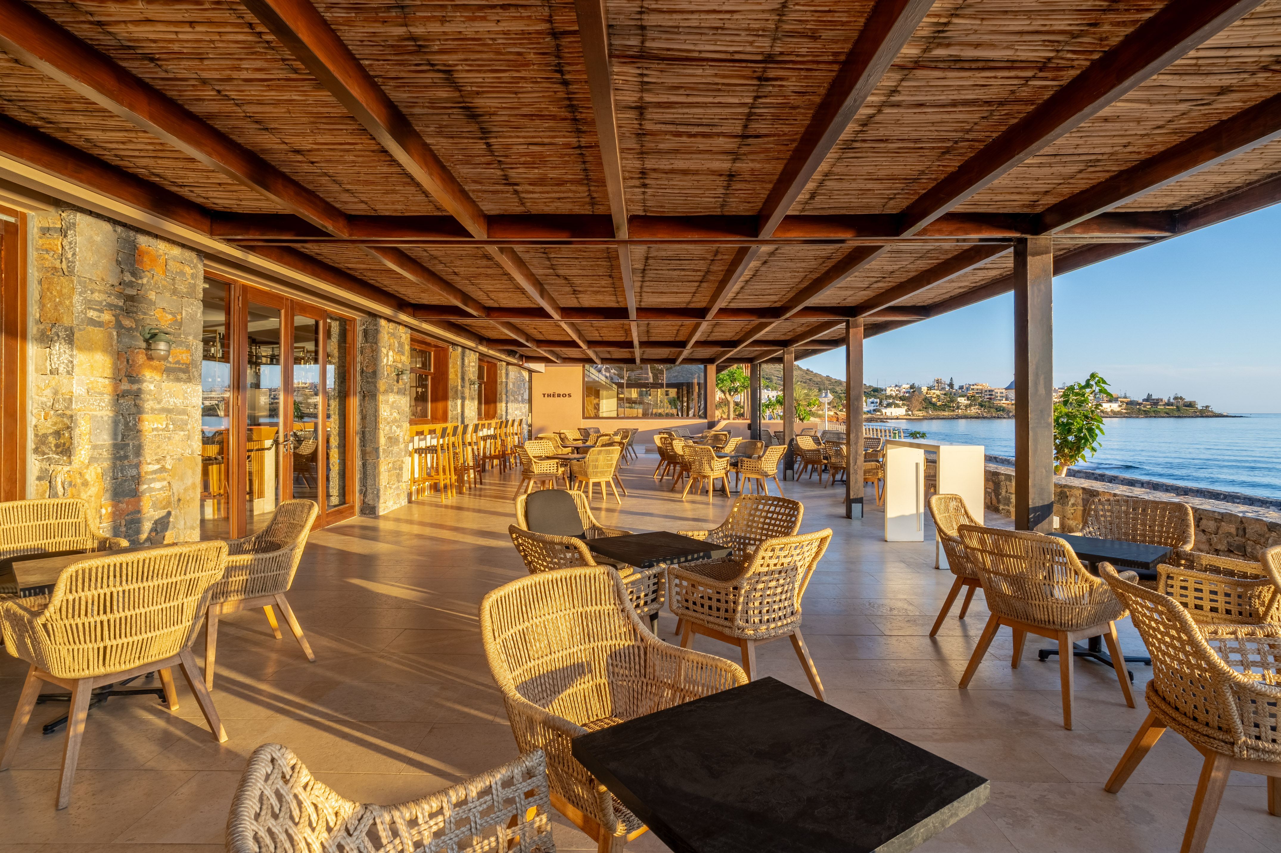 Coastal restaurant patio with woven chairs, wooden ceiling, and sea view.