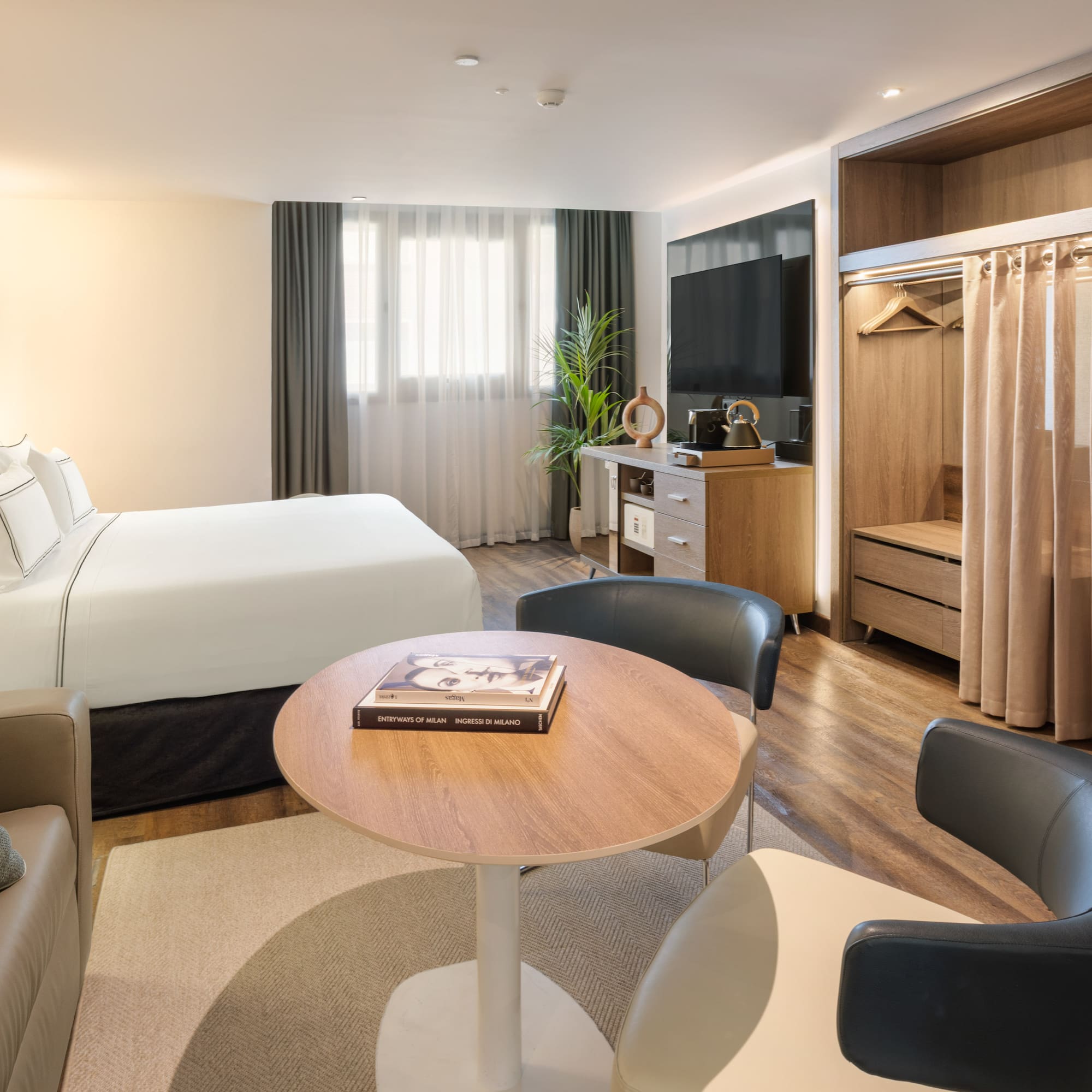 Modern hotel guest room with bed, sofa, TV, and open wardrobe.