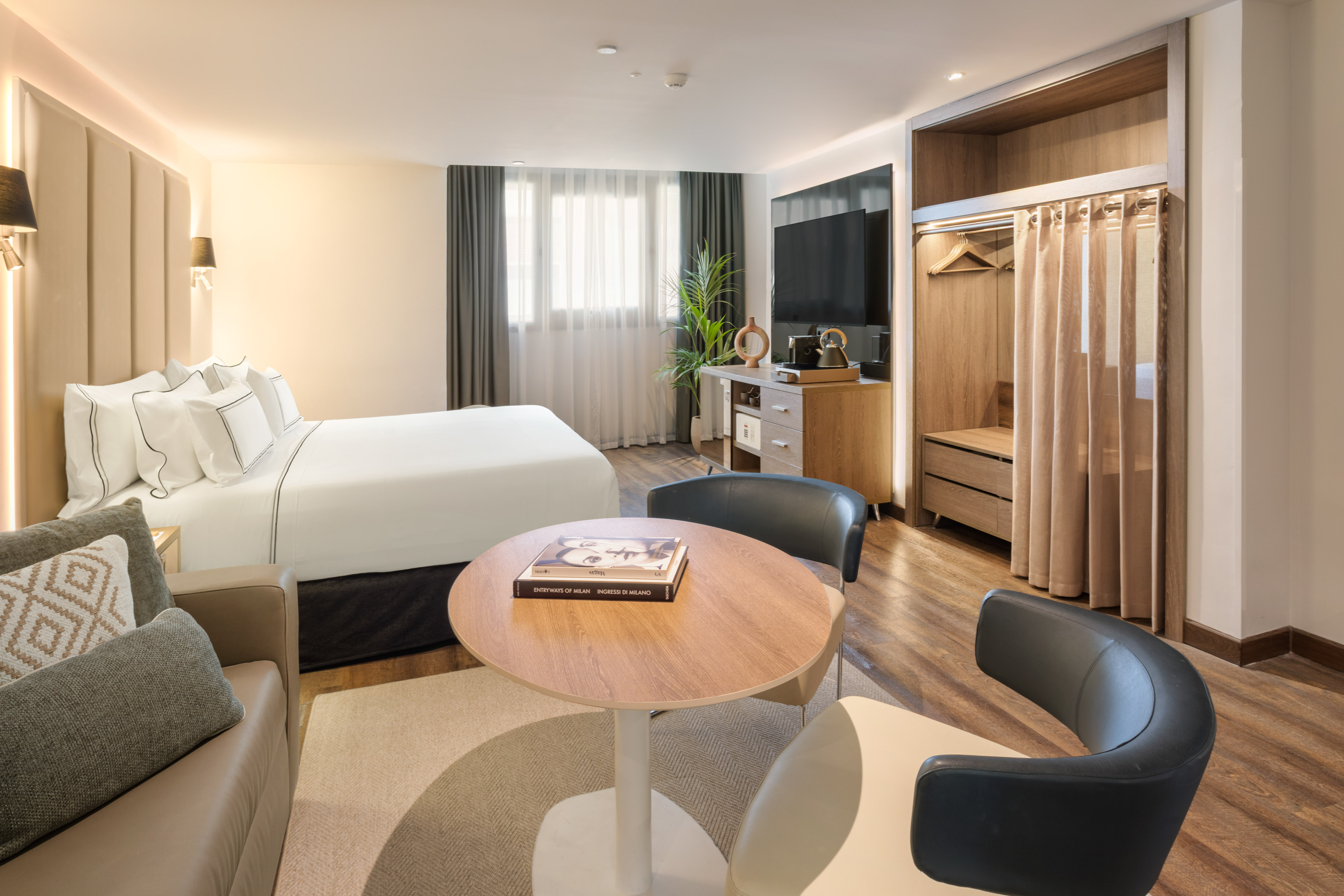 Modern hotel guest room with bed, sofa, TV, and open wardrobe.