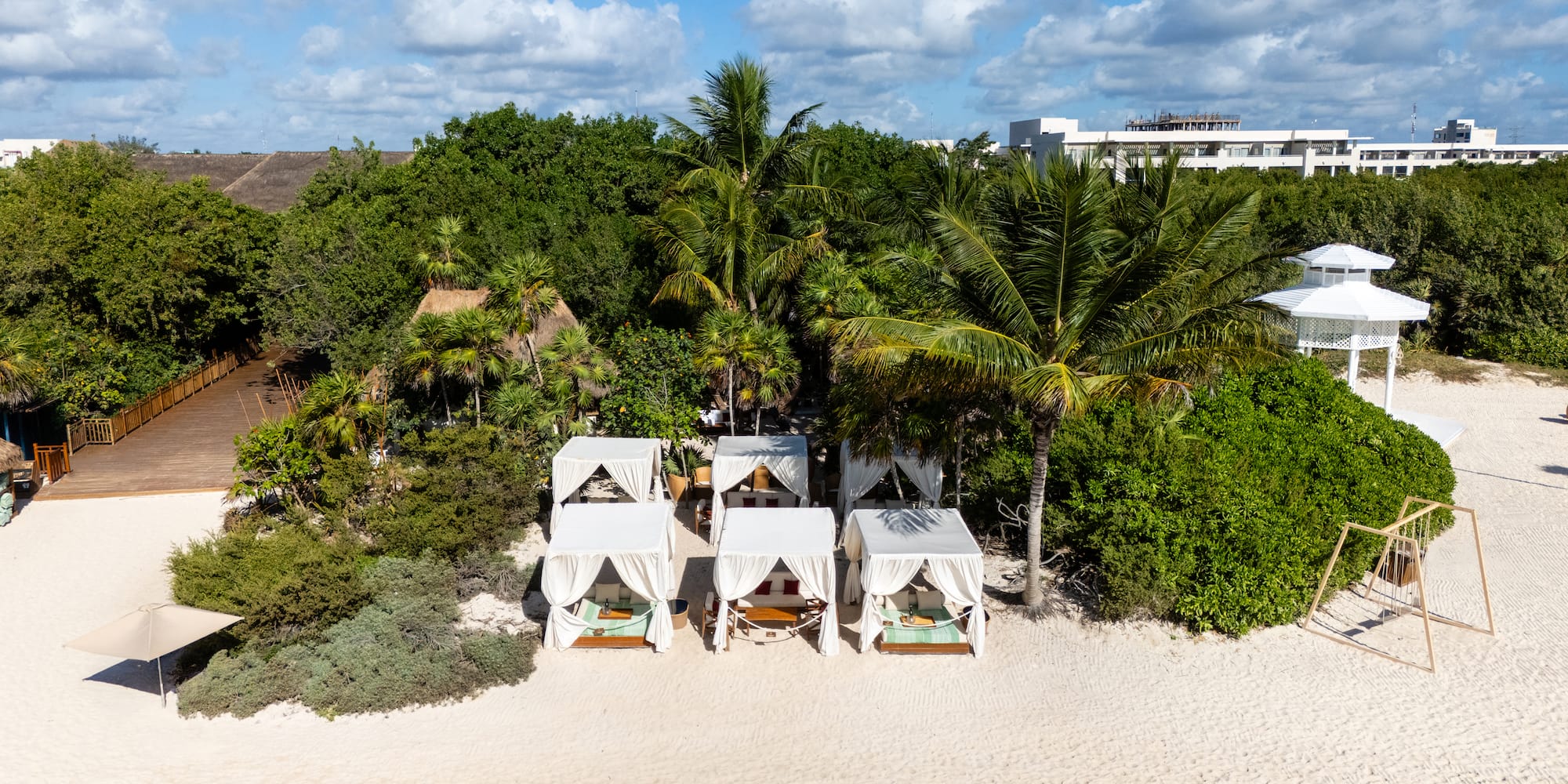 Luxury beach cabanas on white sand, tropical palms, and resort buildings.
