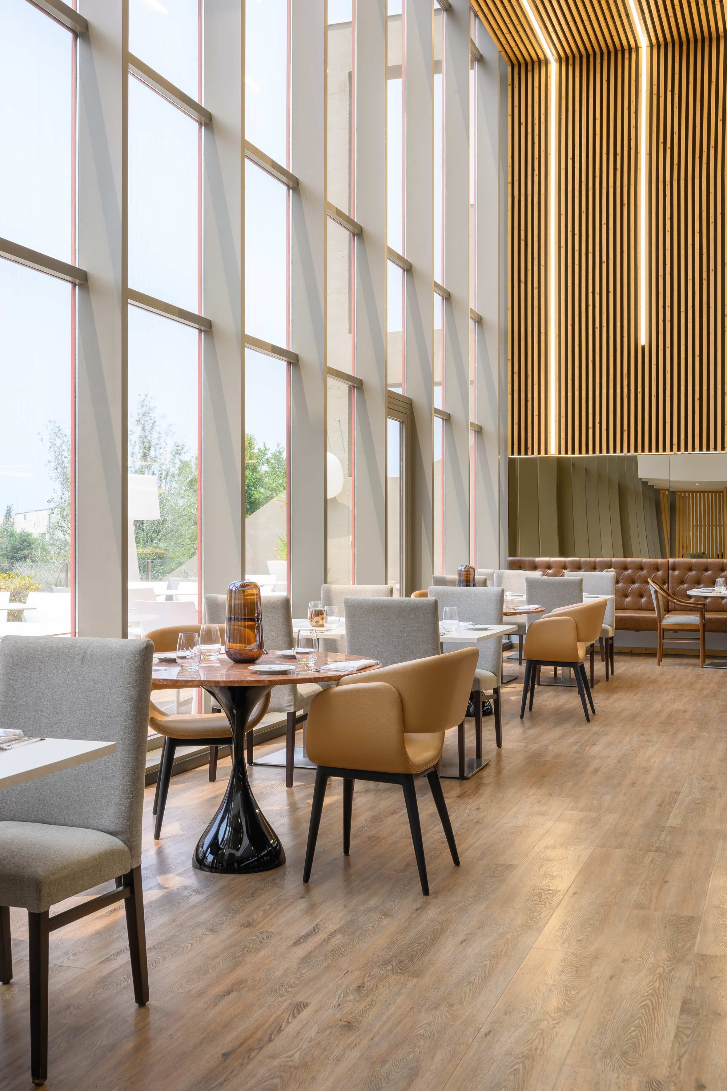 Modern restaurant with large windows, wood slat ceiling, and elegant dining tables.