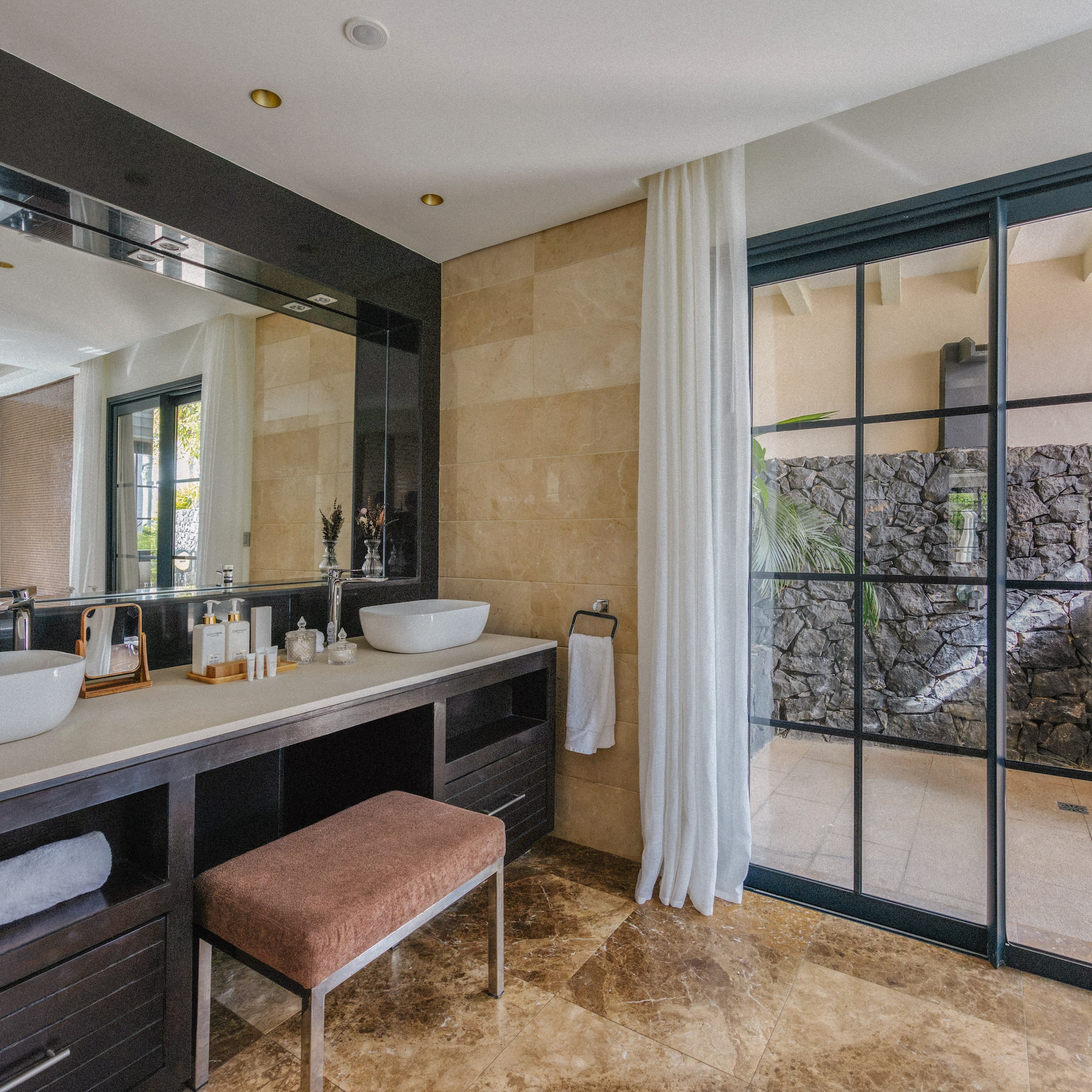 Modern double vanity bathroom with marble, glass door to outdoor stone wall.