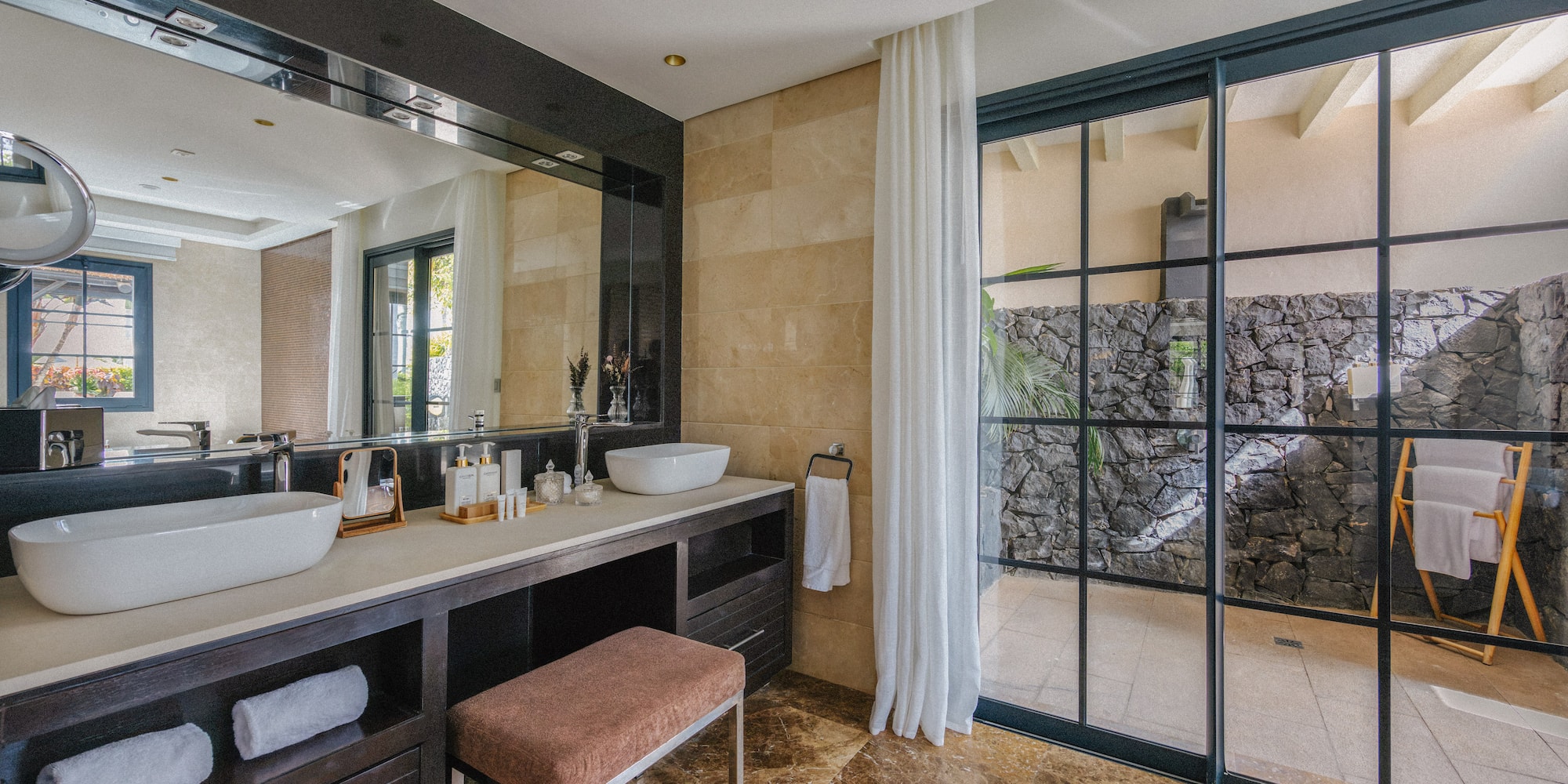 Stylish bathroom featuring dual vessel sinks, dark vanity, marble floor, and outdoor access.