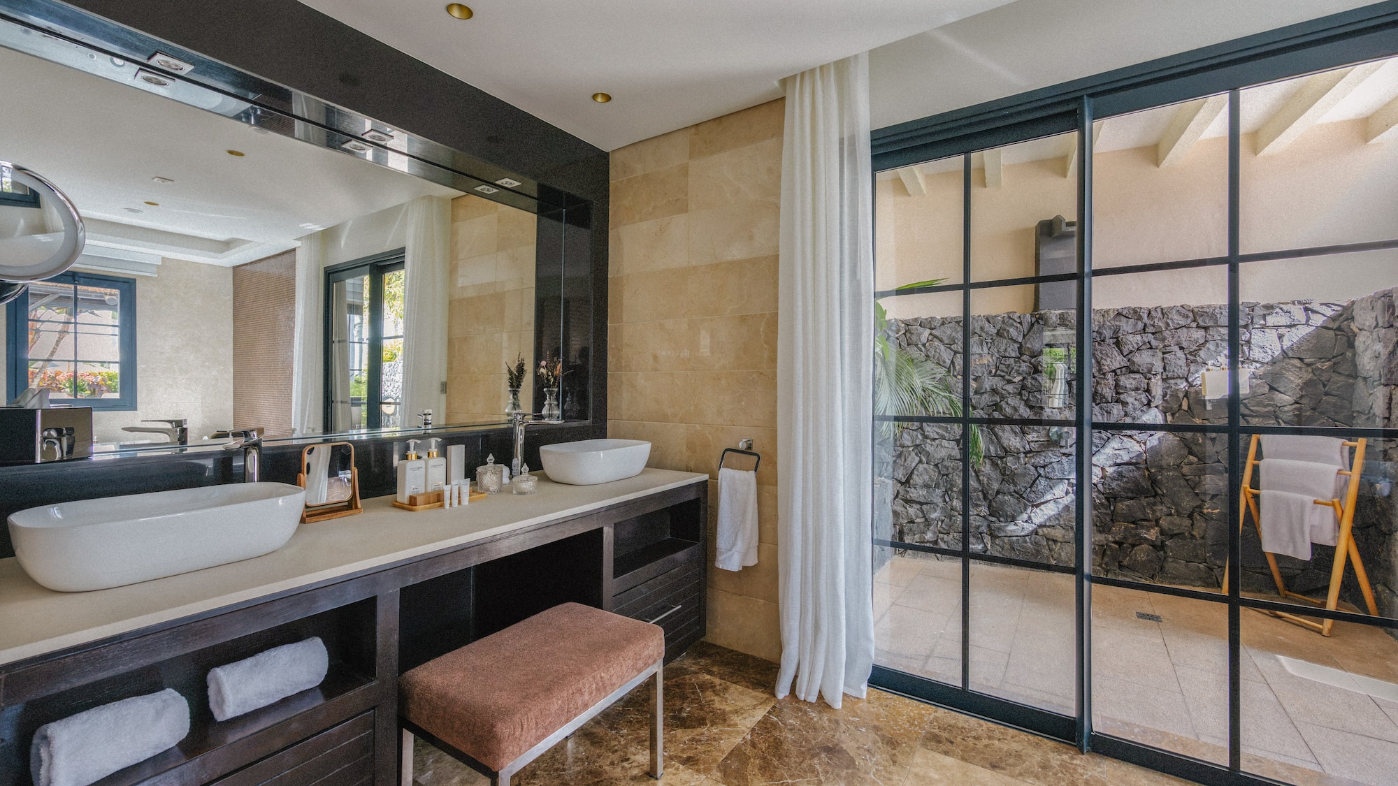 Stylish bathroom featuring dual vessel sinks, dark vanity, marble floor, and outdoor access.