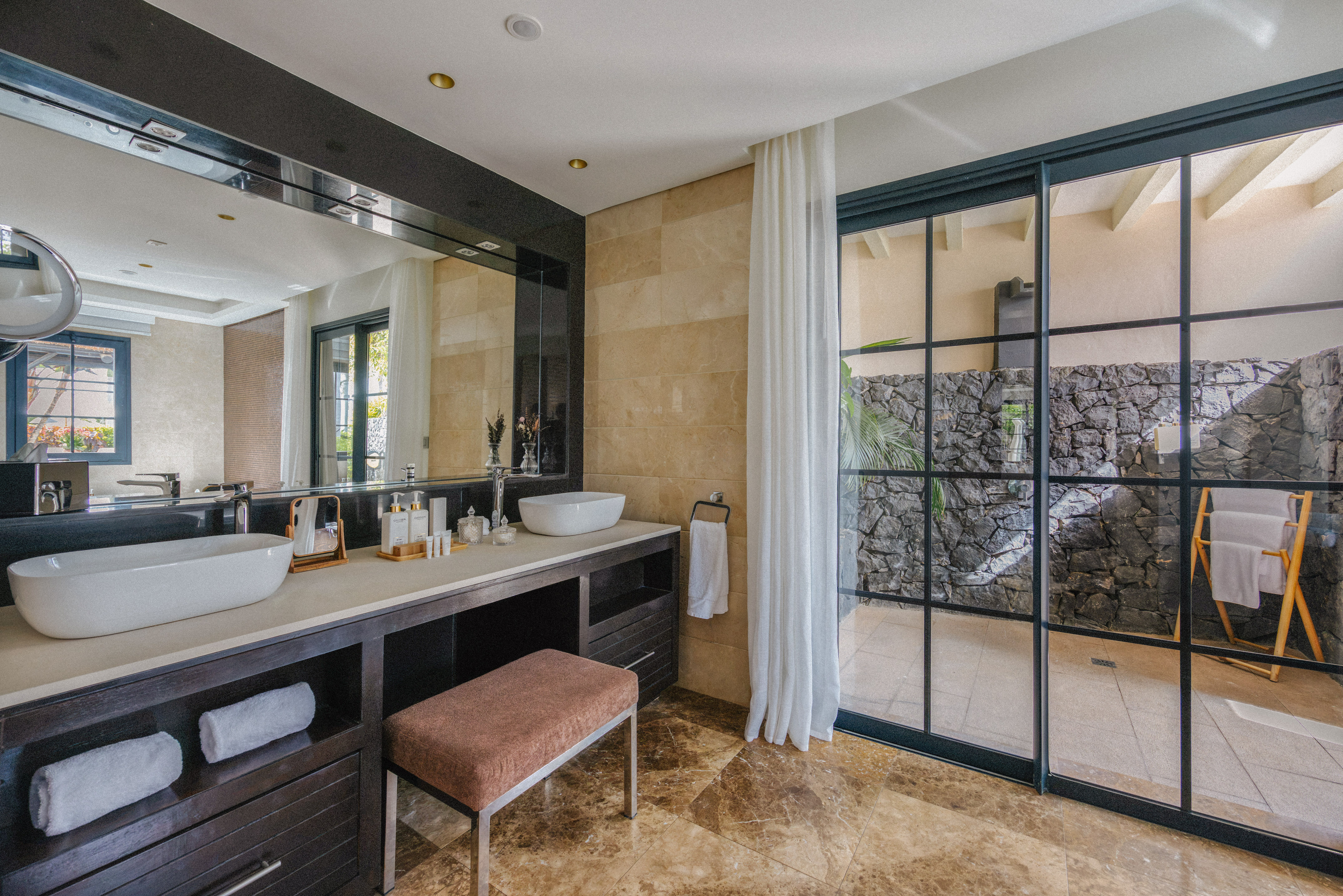 Stylish bathroom featuring dual vessel sinks, dark vanity, marble floor, and outdoor access.