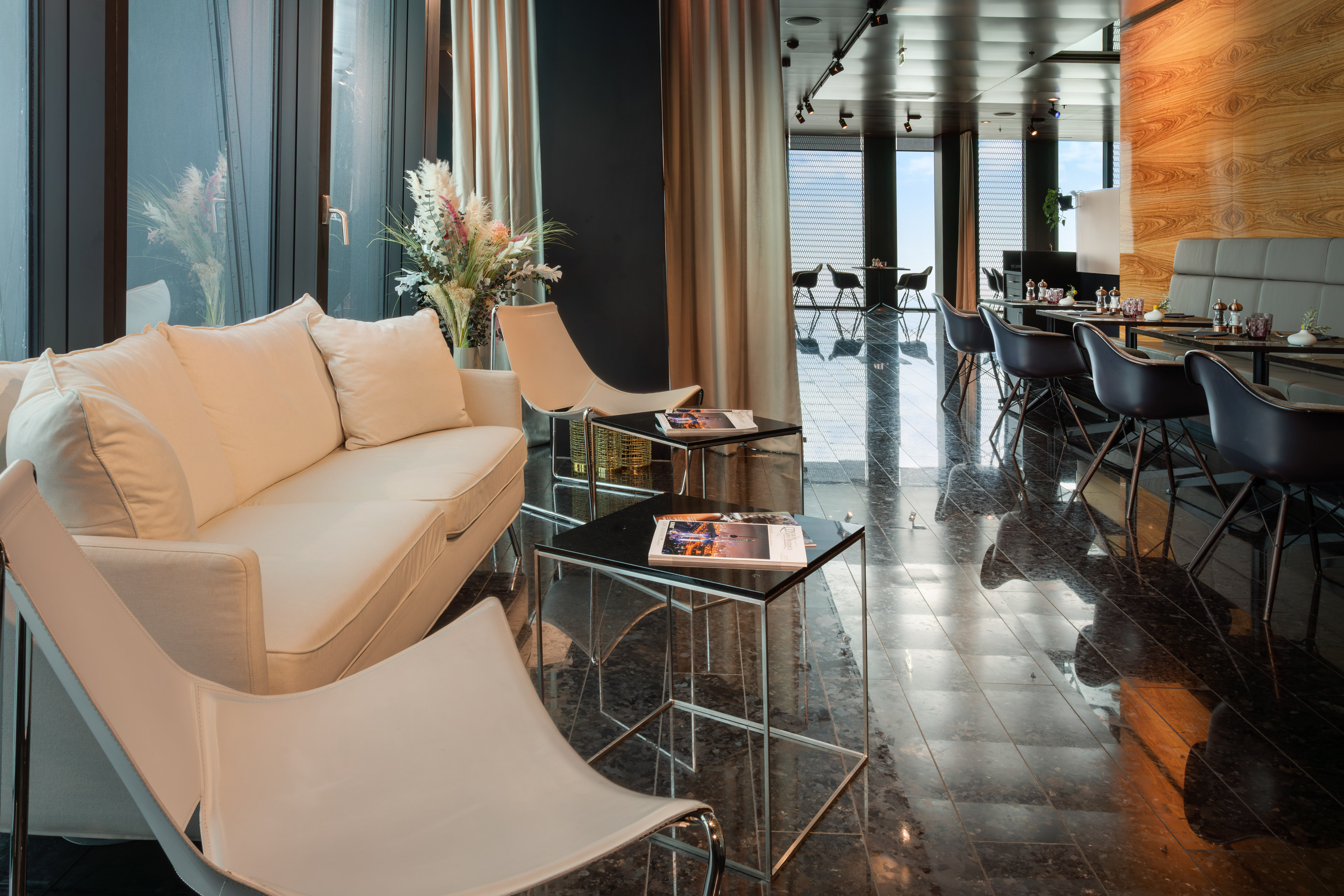 Elegant modern lounge and restaurant with sofa, dining tables, large windows.