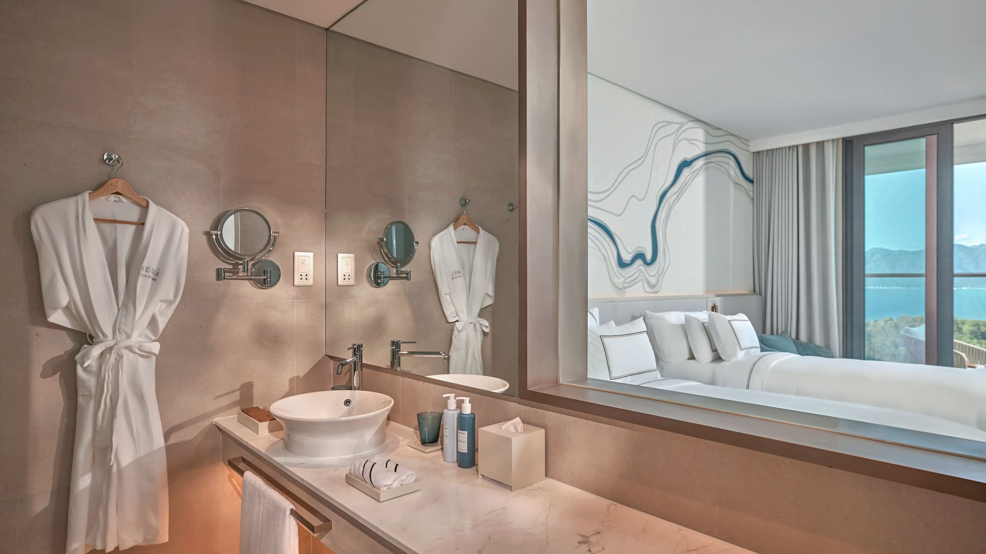 Modern hotel bathroom vanity reflecting bedroom with ocean view.