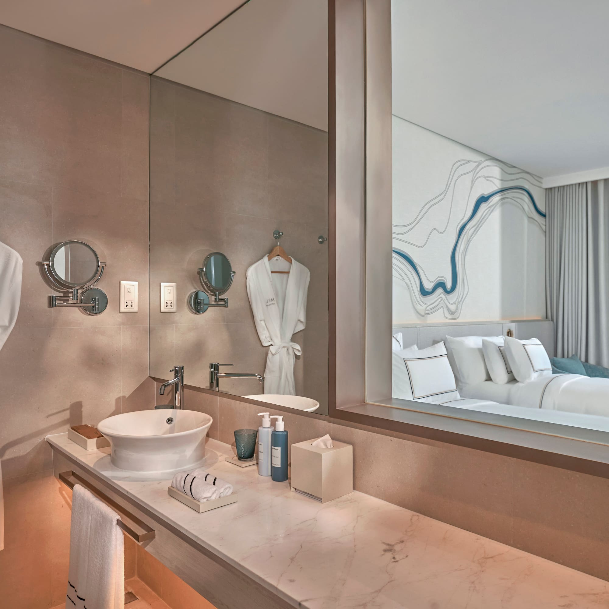 Modern hotel bathroom vanity reflecting bedroom with ocean view.