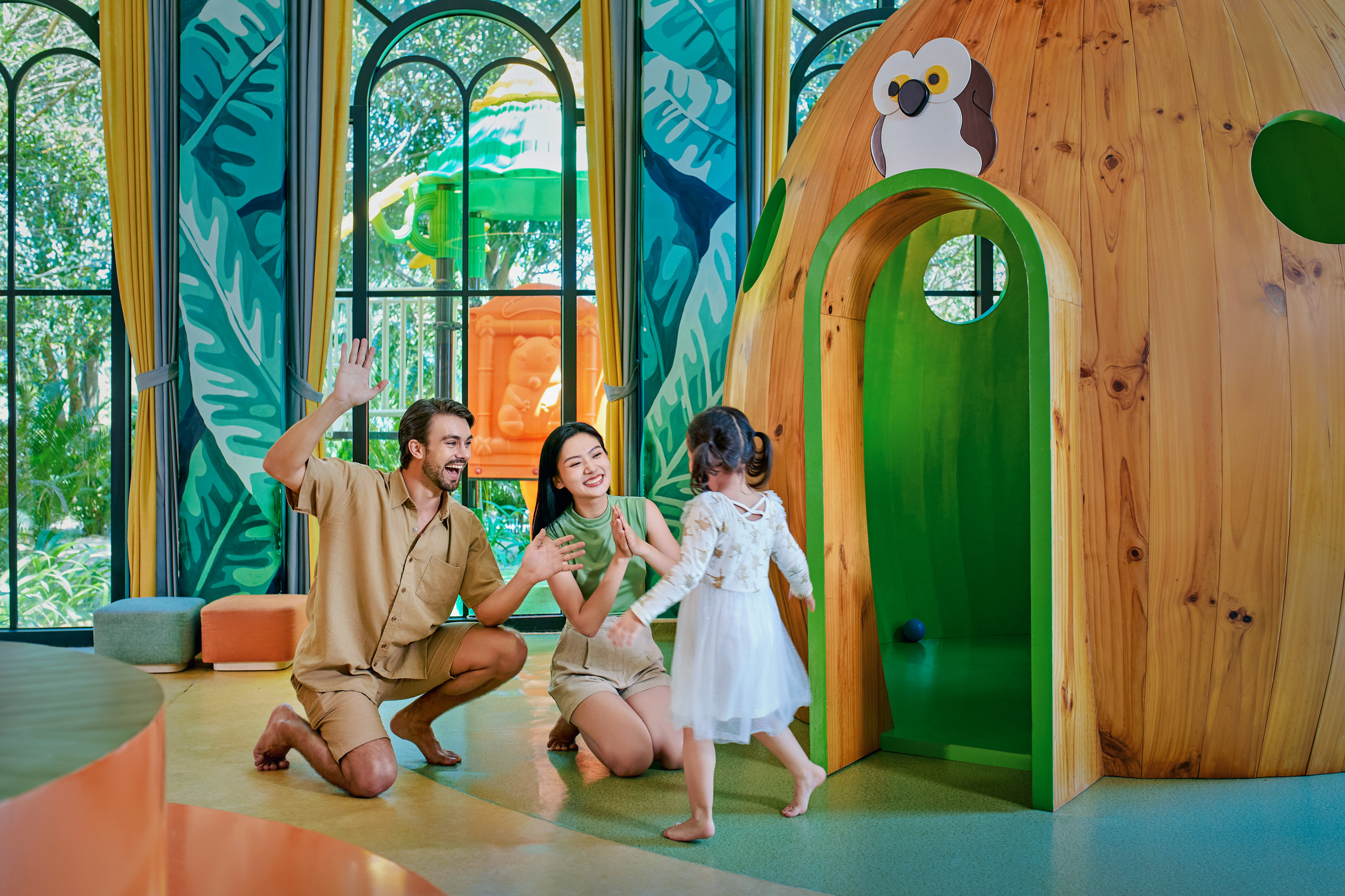 Family playing with child in a vibrant kids' play zone with a wooden treehouse.