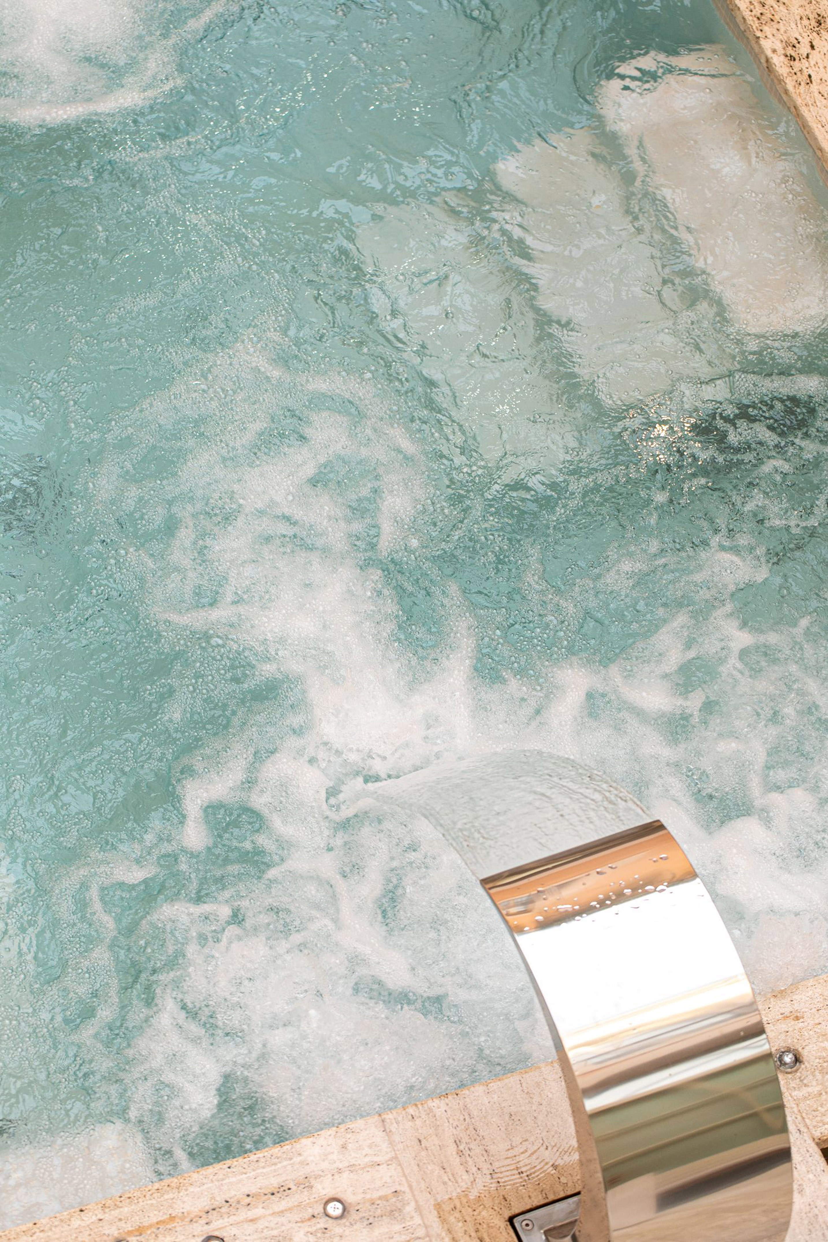 Bubbling turquoise jacuzzi water with a chrome waterfall spout.