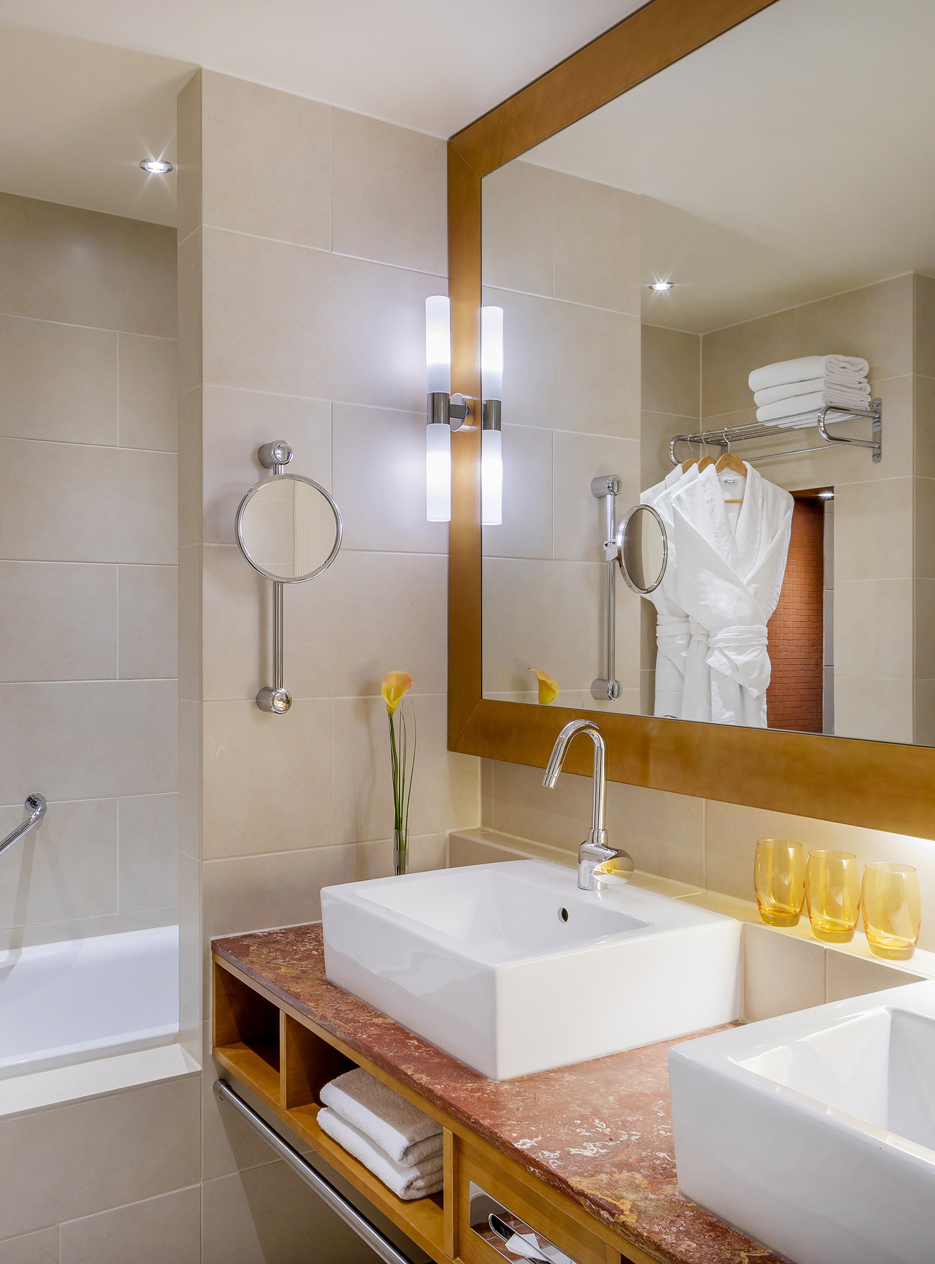 Modern hotel bathroom with marble double vanity, twin sinks, mirror, and robes.