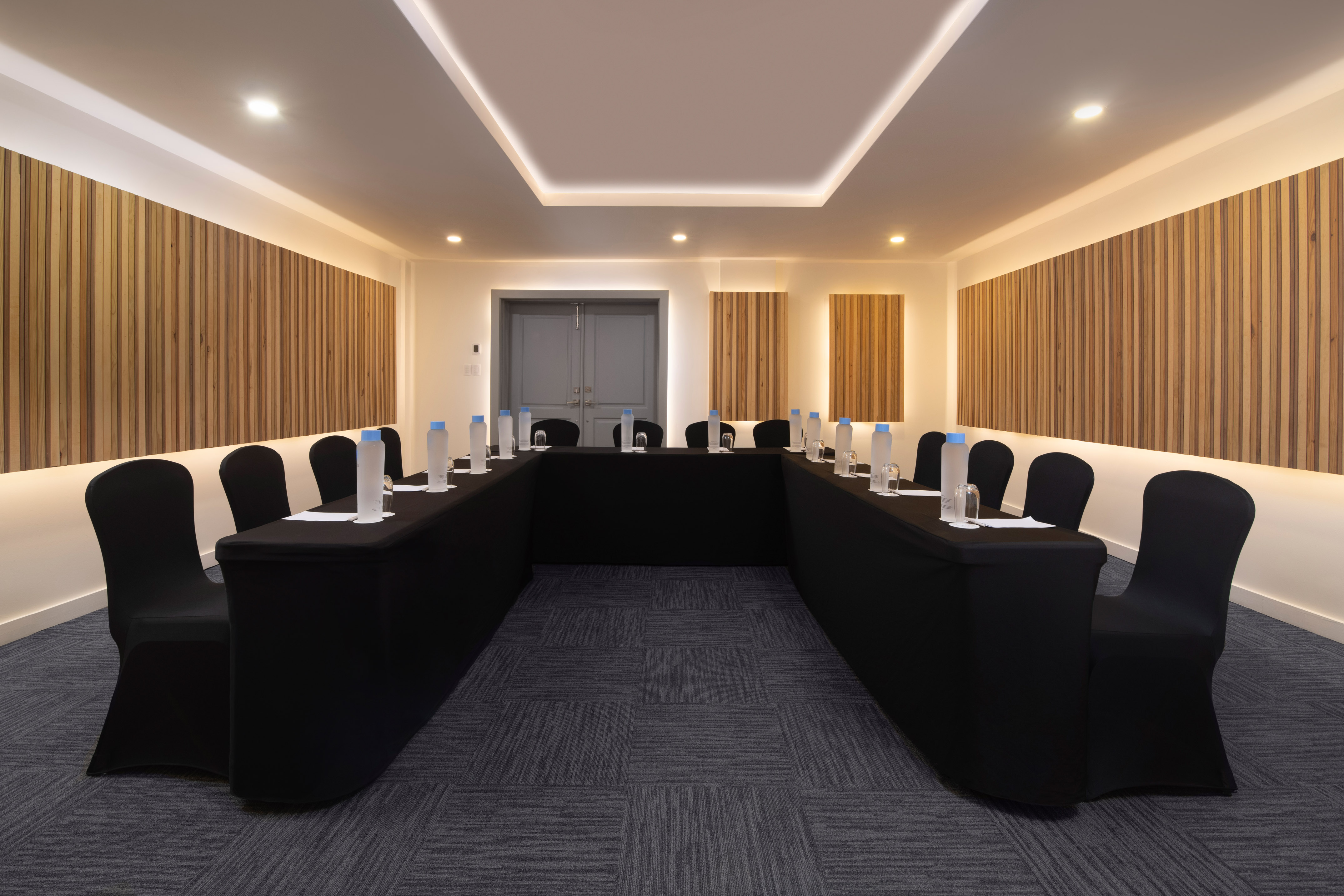 U-shaped conference room with black table and chairs, wood paneling, and modern lighting.