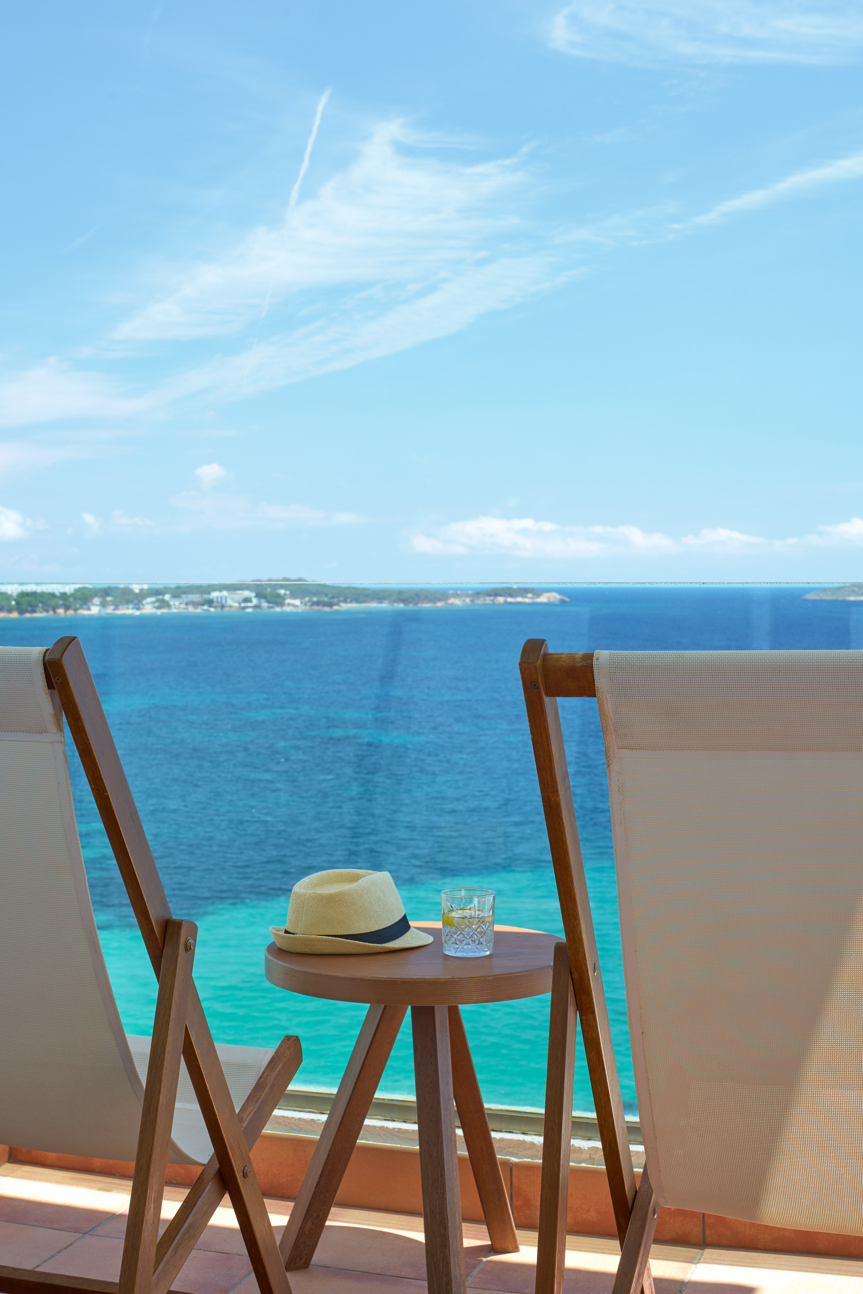 Balcony with lounge chairs, straw hat, drink, clear blue ocean view.