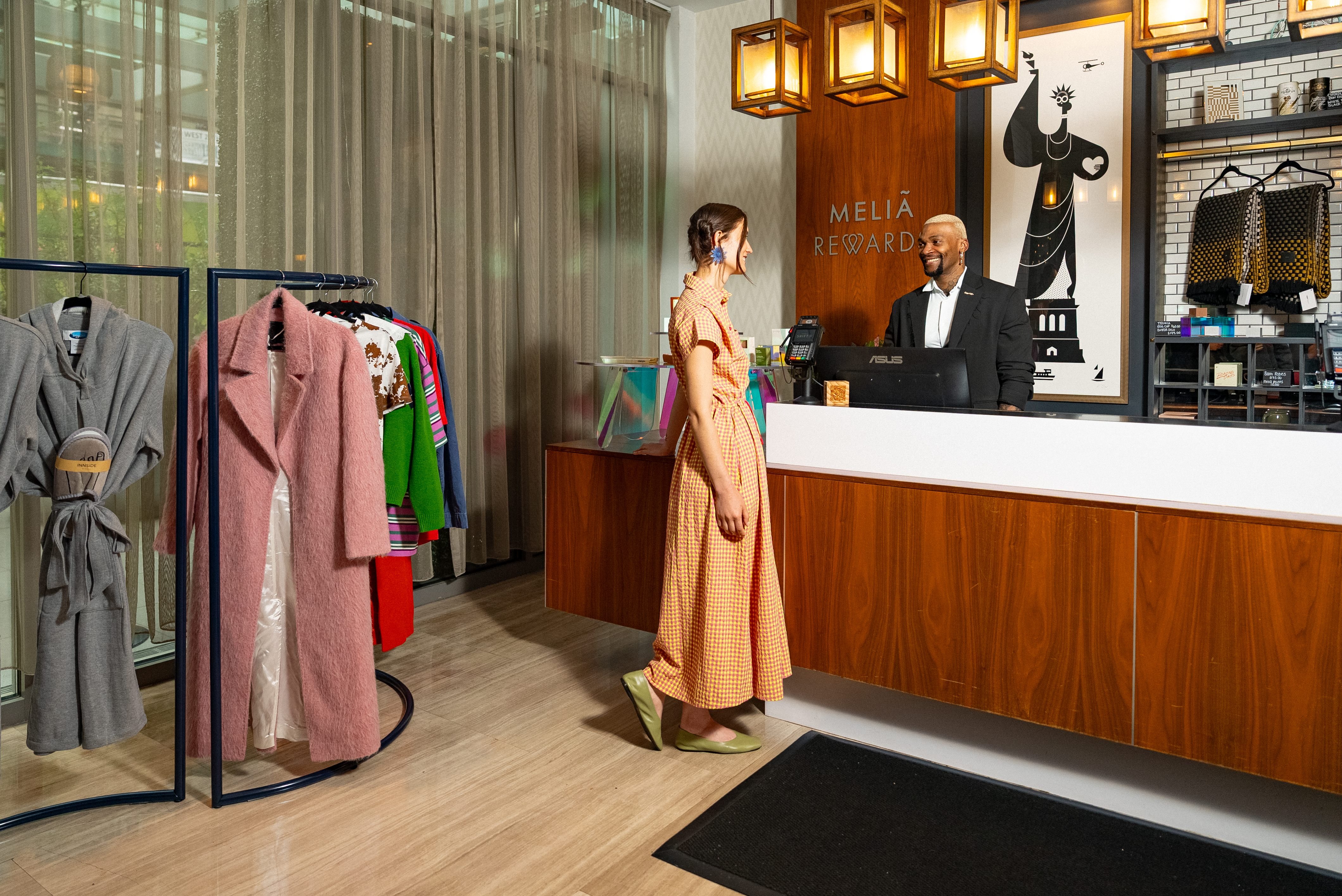 Melia Rewards hotel reception with guest, smiling staff, and fashion items on display.