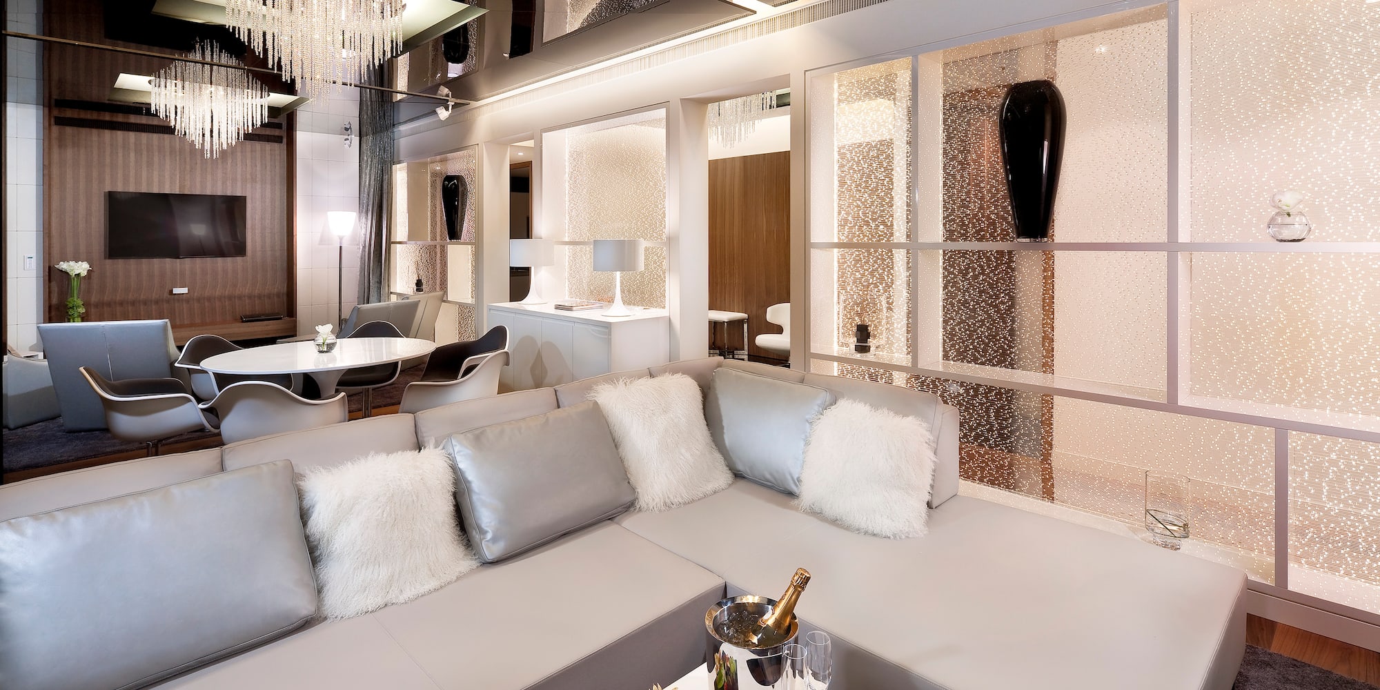 Luxury hotel suite living room with grey sectional sofa, champagne, modern design.