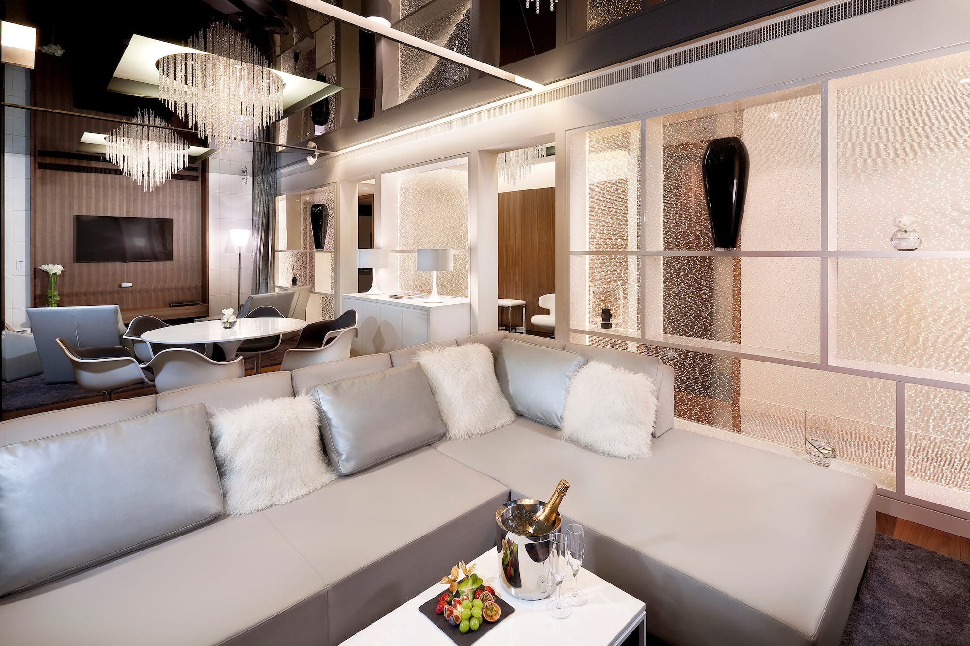 Modern luxury living room with sleek grey sofa, champagne, and chandelier.